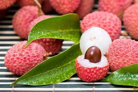 red lychee with green leaves. One lychee has been completely peeled (white) and one has been partially peeled and th fruit has been removed from the top half revealing the brown seed inside.