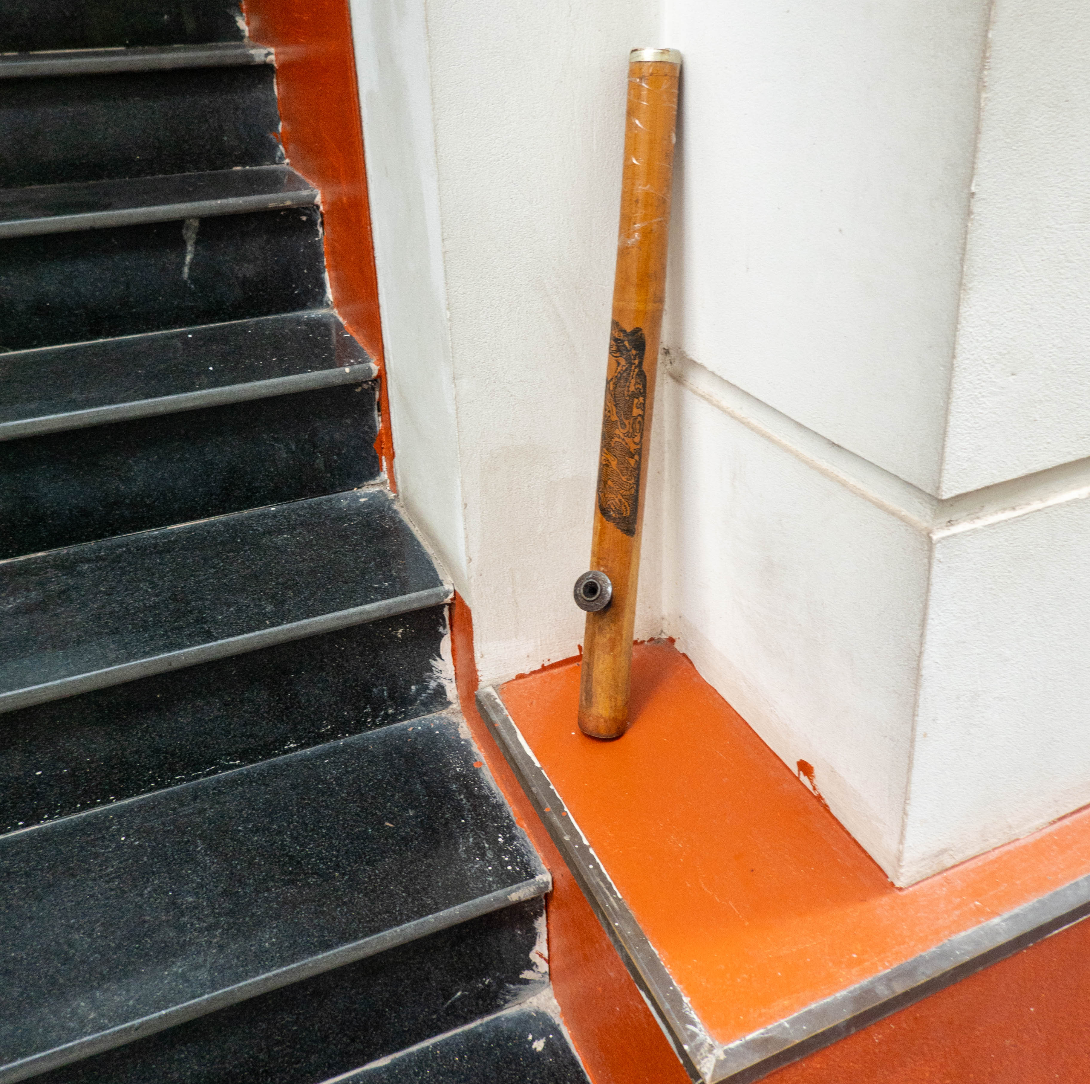 pictue of long bamboo pipe leaning against wall on right side of picture. black steps are going up on left side of picture.