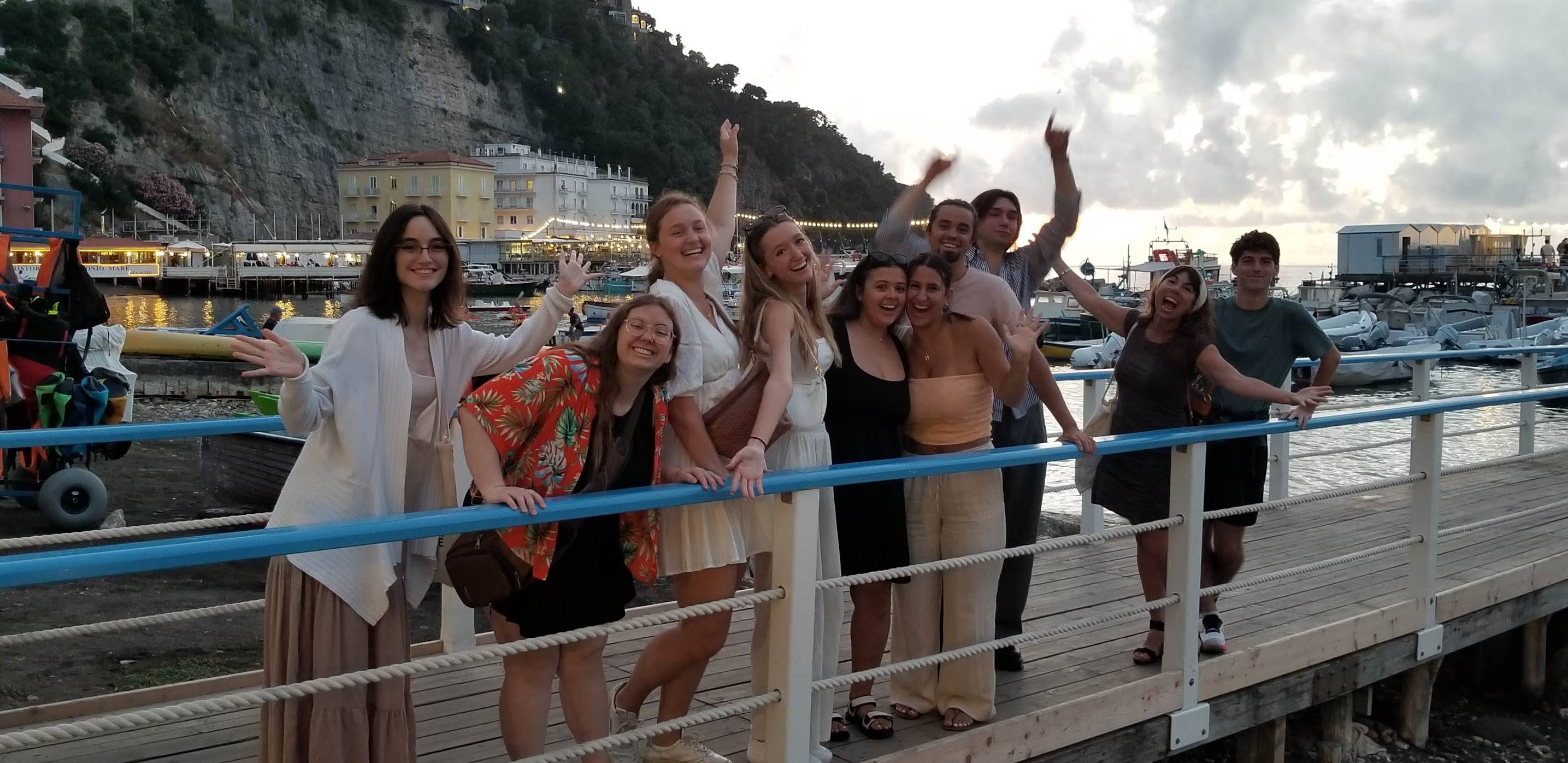 group of people standing on a pier, cliffs, water, trees in background