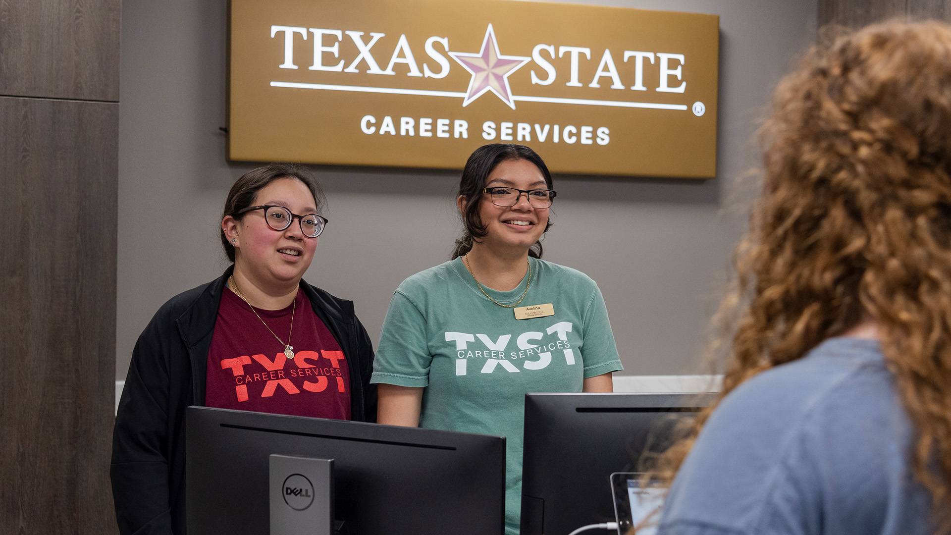 Two student workers at the Texas State Career Services desk talking to another student