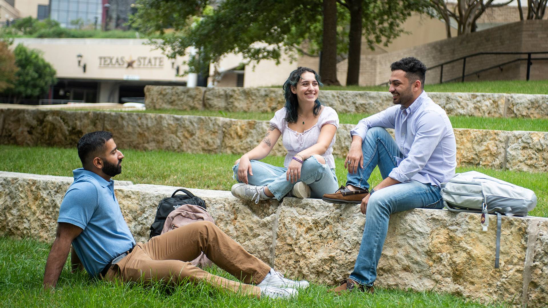 Three students sitting outside on campus laughing and talking