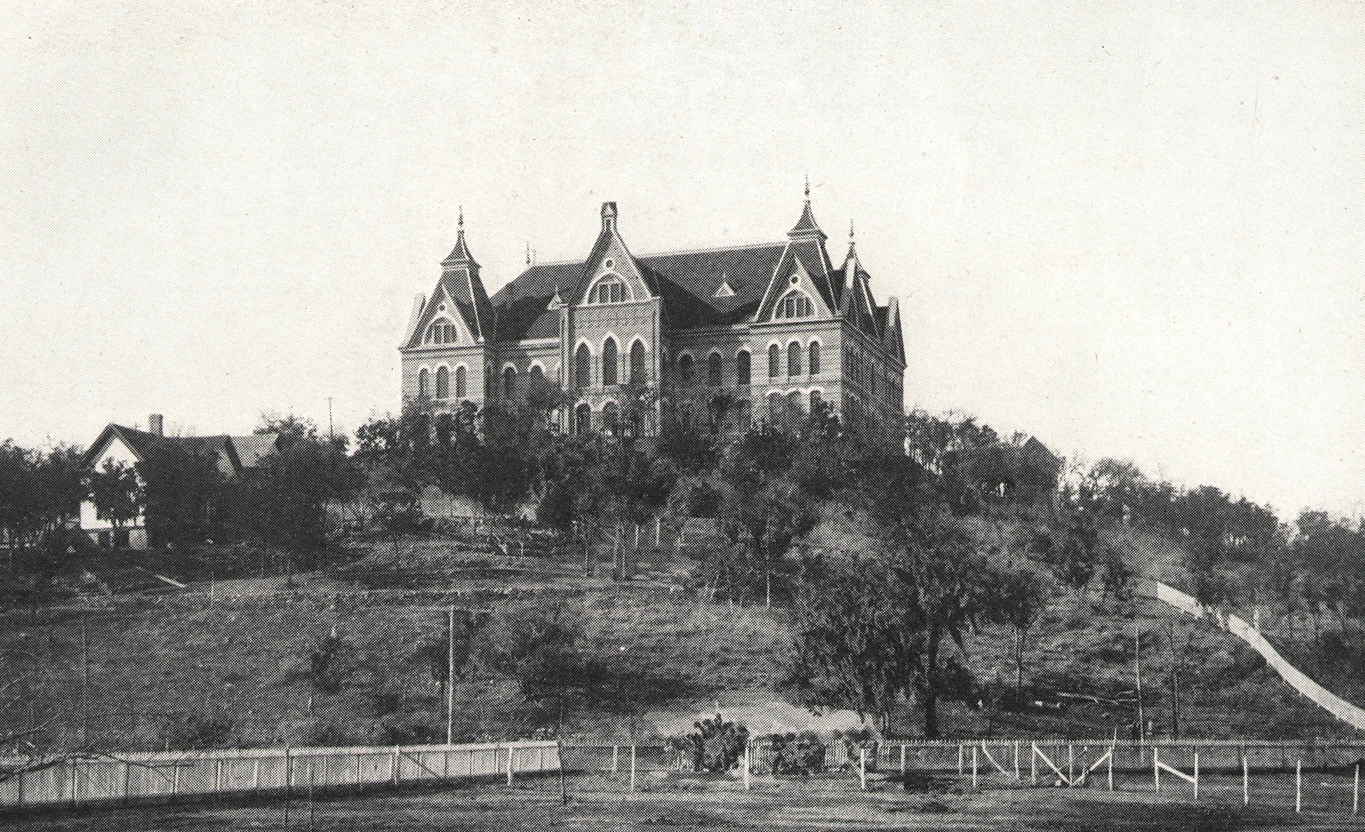 Black and white historical photo of Old Main, the first building at TXST, at the top of a hill.