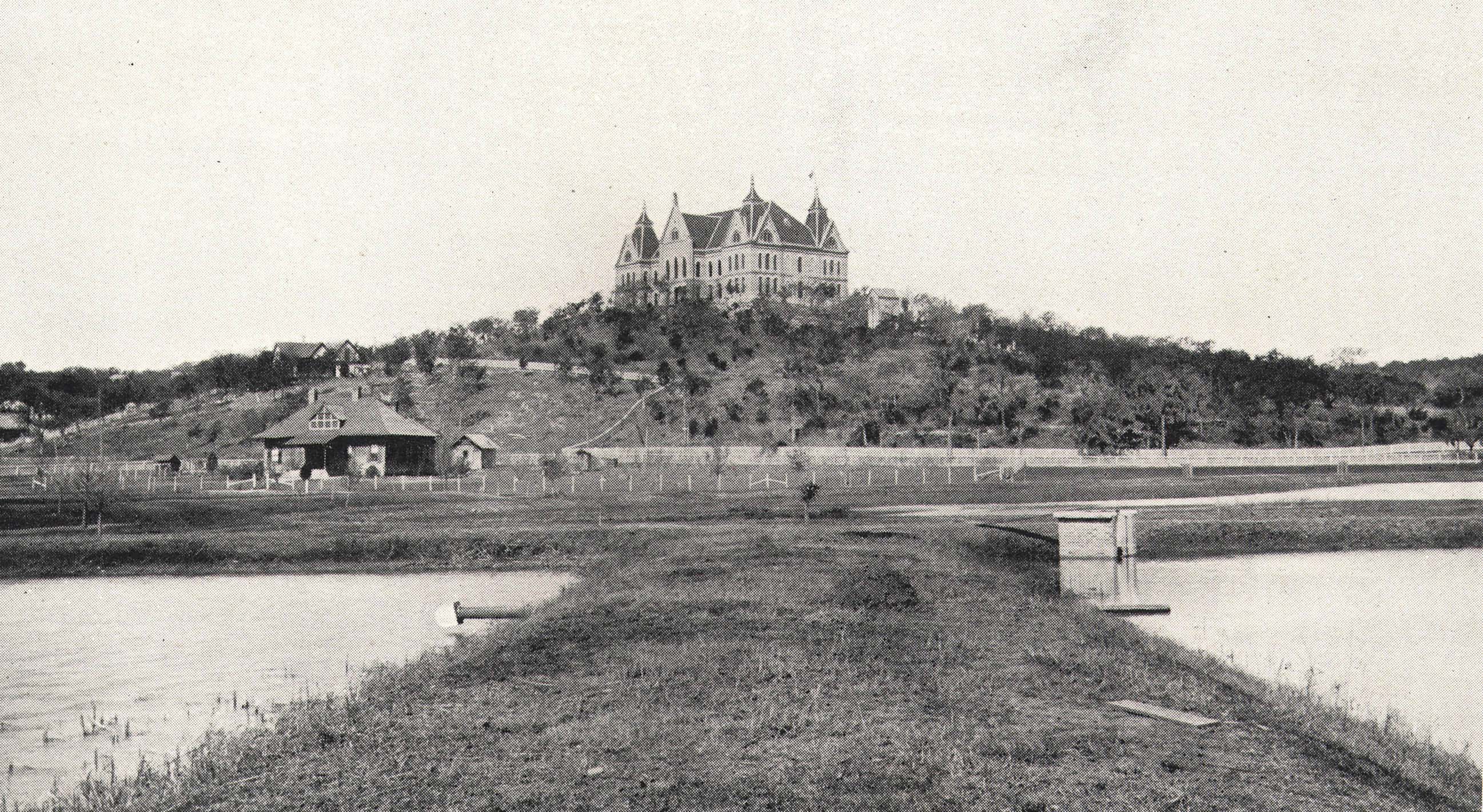 Black and white historical photo of the old fish hatchery in front of the Old Main building.