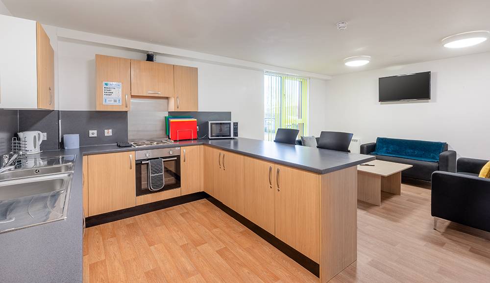 Kitchen with wooden cabinets, grey granite countertops and stainless-steel appliances; featuring furnished living room at UHI inverness residence hall.