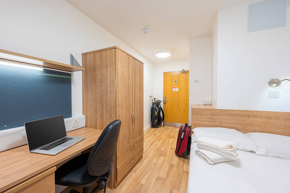  Single room at UHI Inverness residence hall furnished with bed, dresser, desk, and chair.