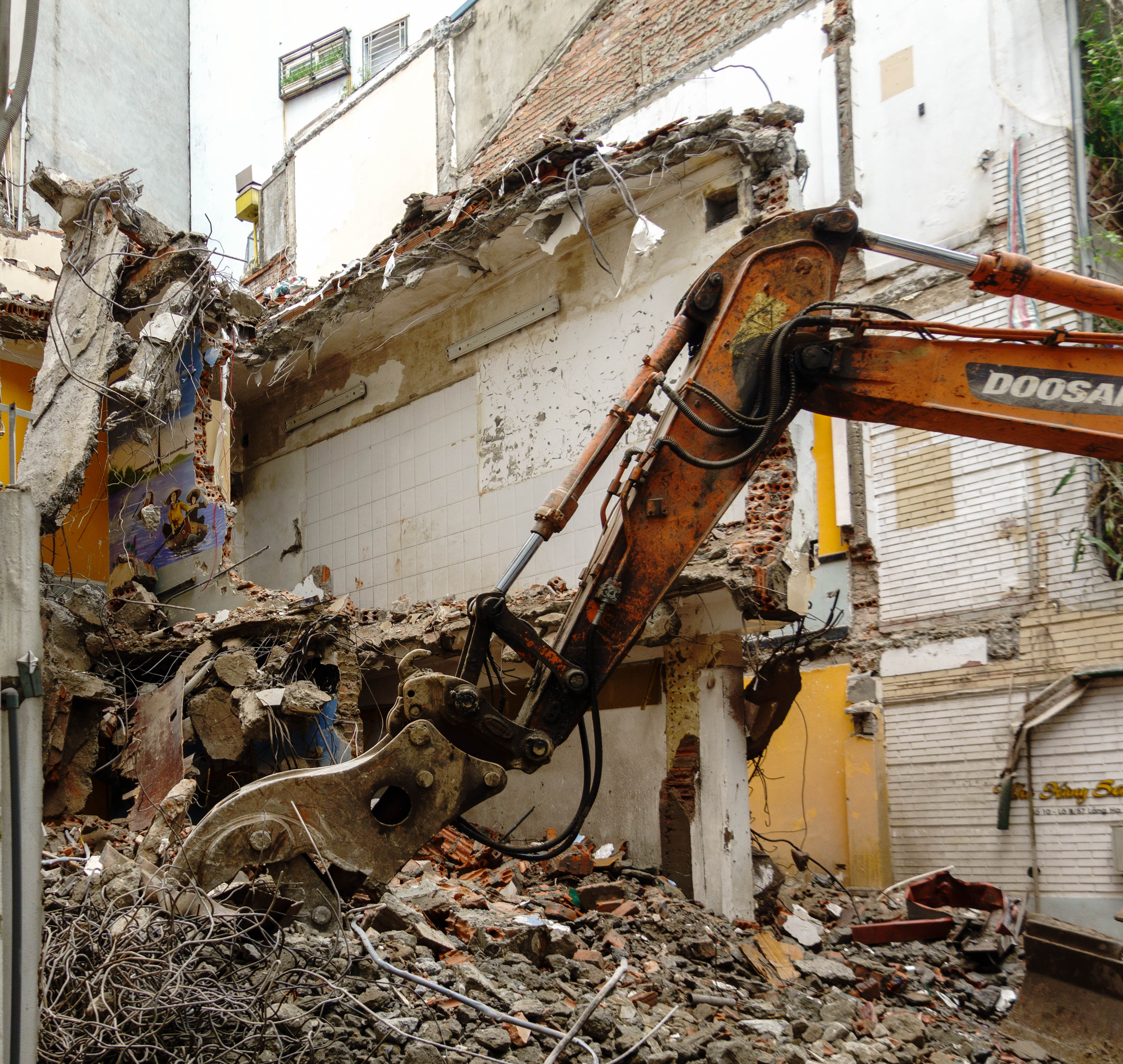 picture of demolished building and the arm of a large backhoe is resting in rubble in the forground