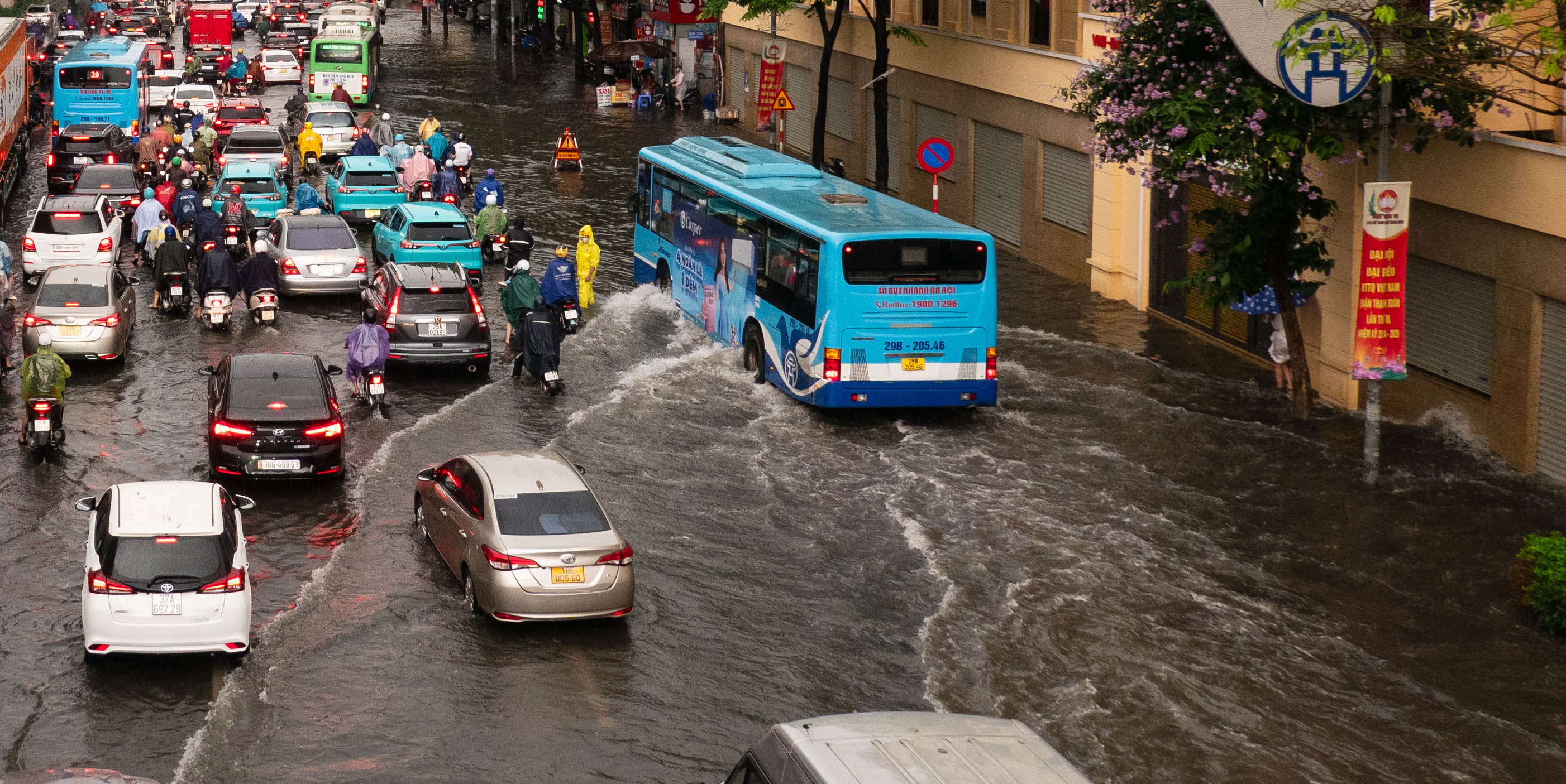 Traffic in deep water. Blue bus ion the right. there is a man dressed in yellow standing in the water near a warning sign.