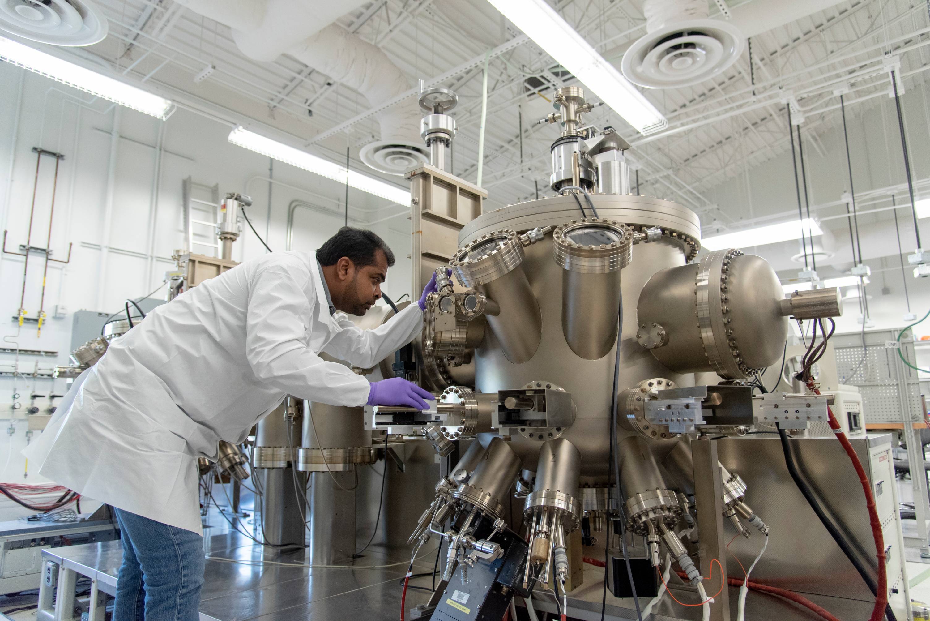 A person in a white lab coat inspecting a large machine made of stainless steel.