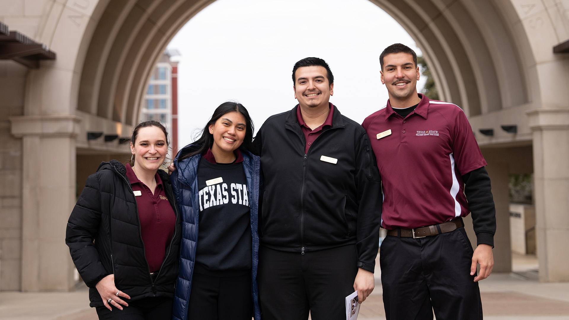 Four staff members posing for a photo in front of the Texas State arch