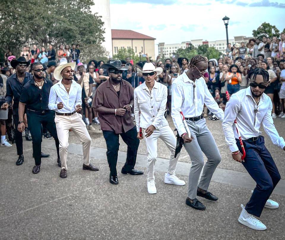 Men of Kappa Alpha Psi congregated in the LBJ Student Center and holding up their organization's hand signs