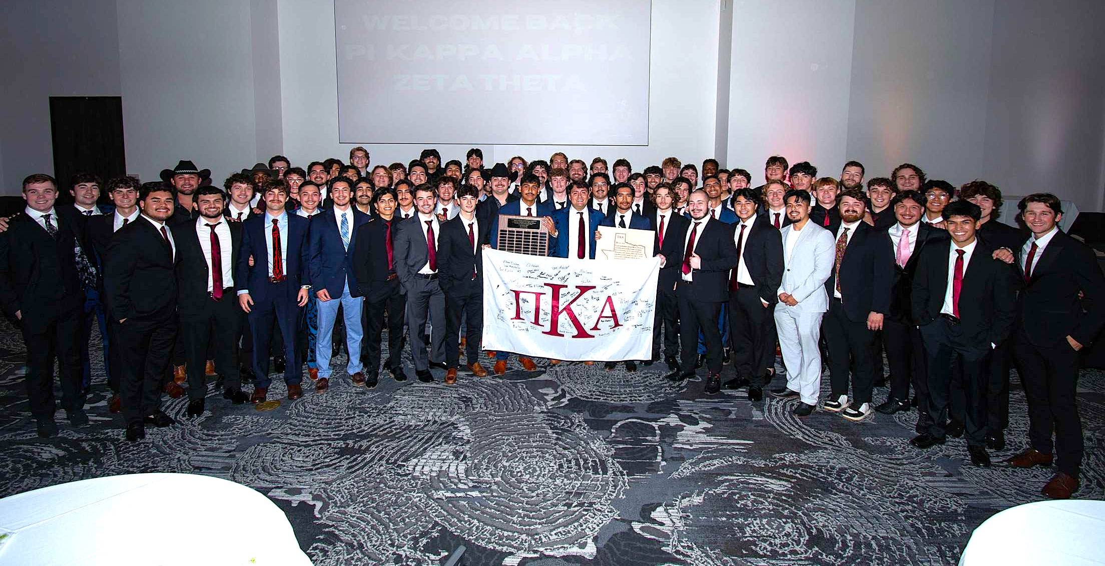 Six men of Pi Kappa Alpha stand behind their table/organization banner wearing suits with ties