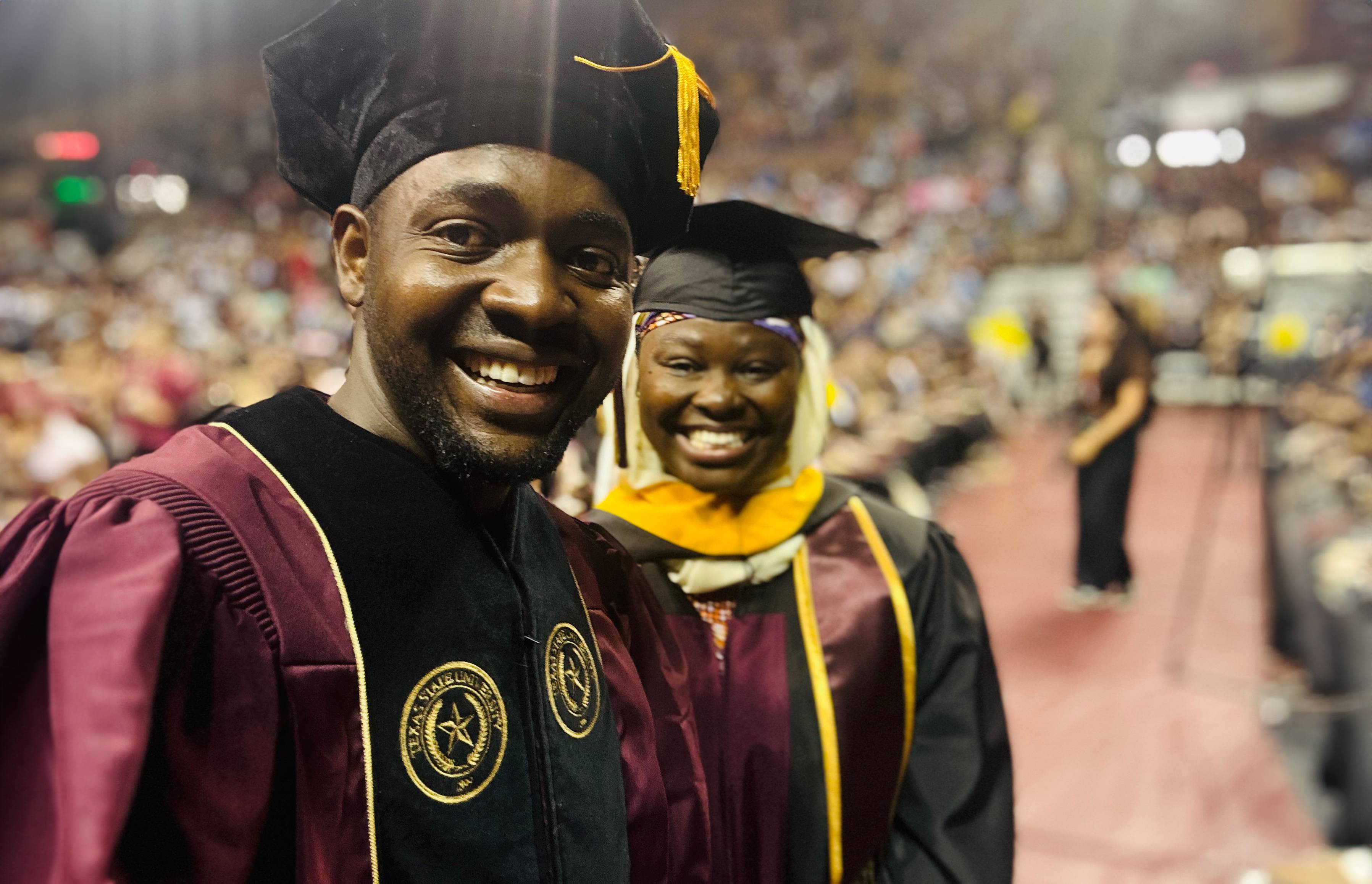 two graduate students pose for a photo at a commencement ceremony