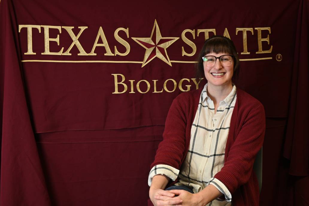 Dr. Davenport seated in front of a Texas State Biology backdrop