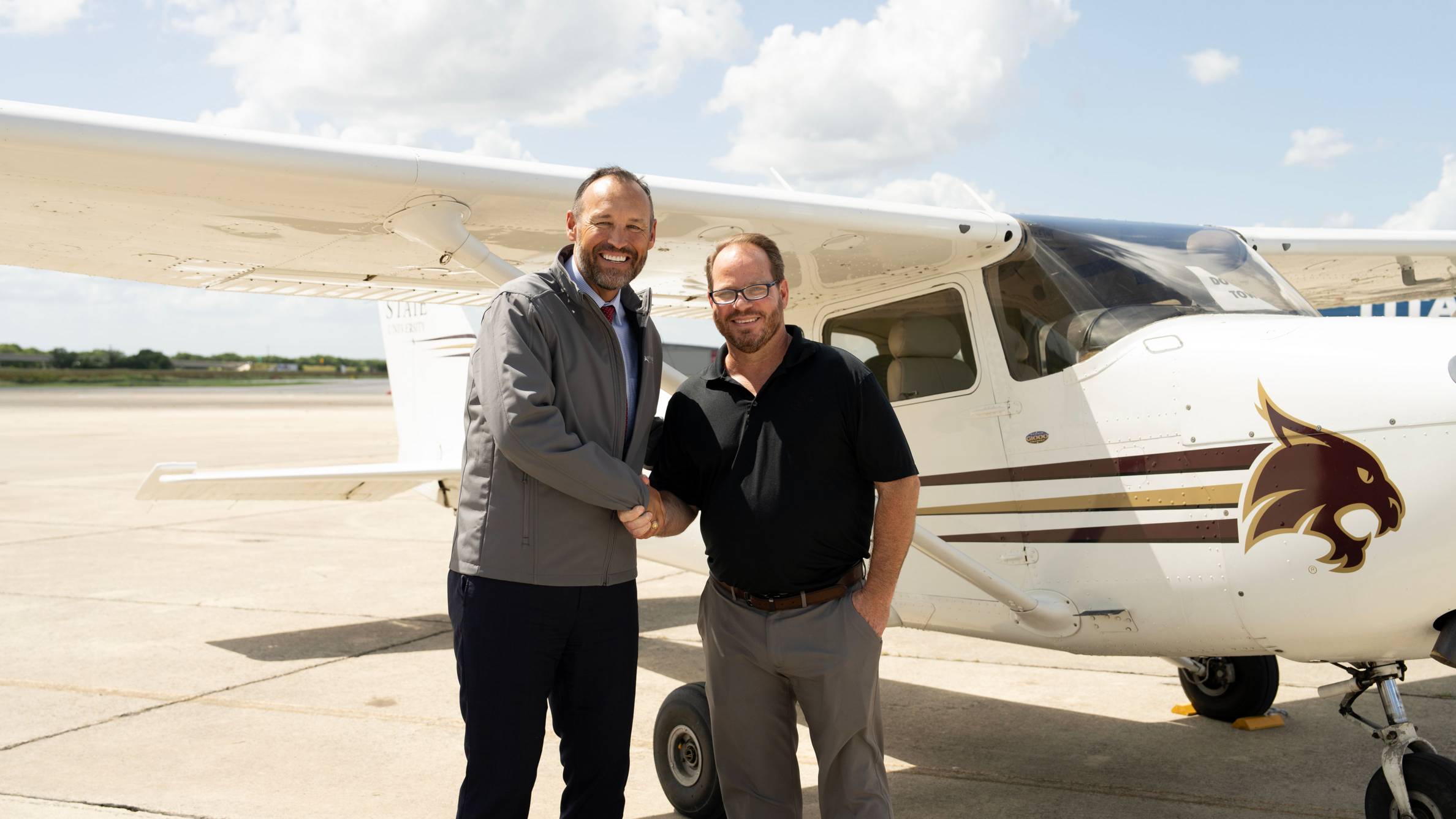 President Damphousse (left) poses for a photo with a Coast Flight executive in front of a TXST-branded plane.
