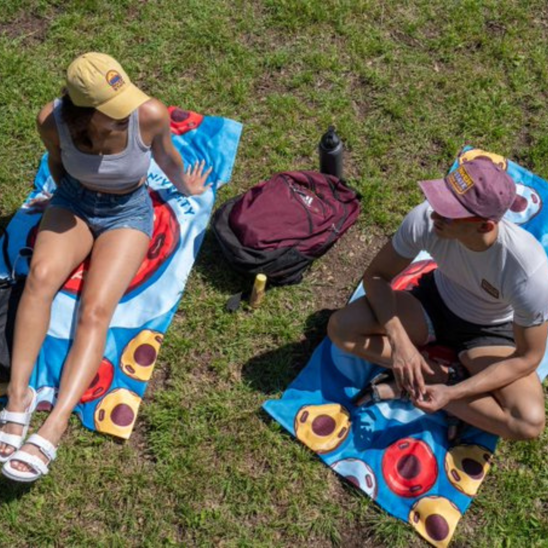 TXST students sitting on River State towels at the San Marcos River with River State merch