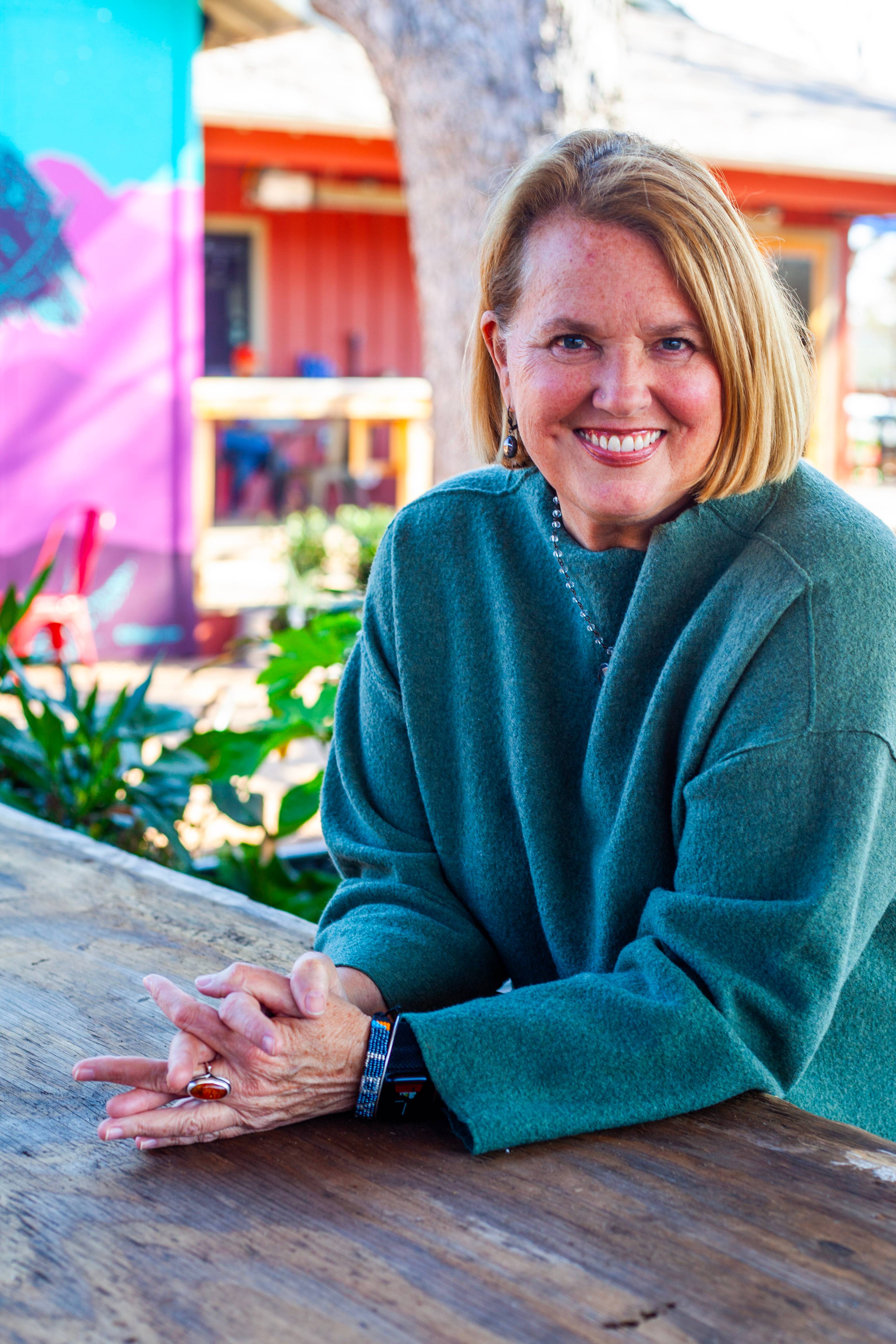 woman with blonde hair sitting at table and smiling at camera wearing a green sweater