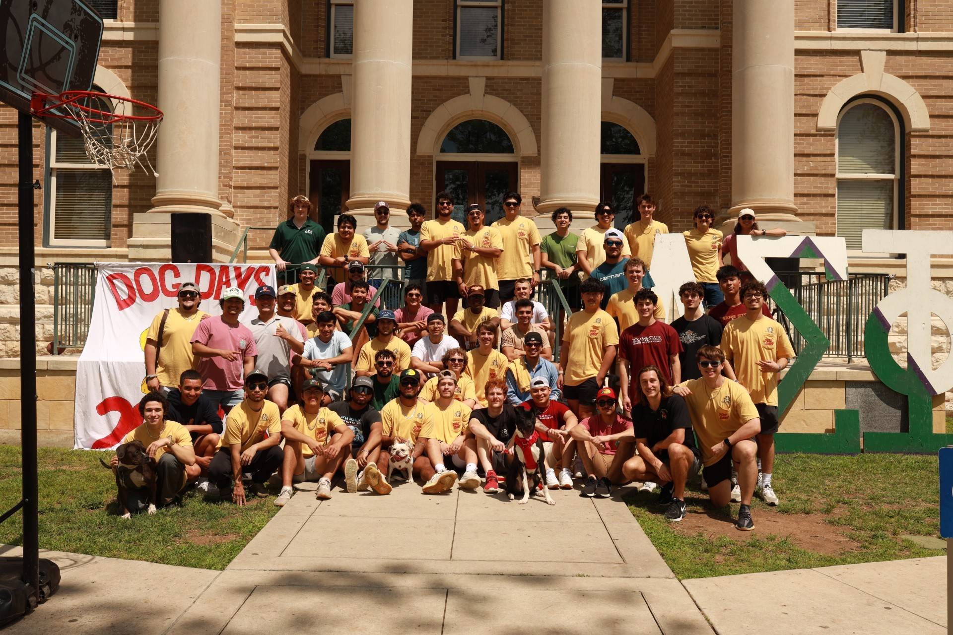 Men of Delta Sigma Phi pose in the Quad in front of their letters. Two dogs are also in the photo.