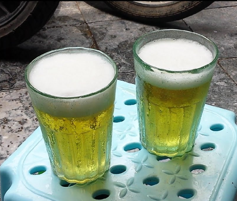 two glasses of beer with foam on top, in translucent green, heavey glass, glasses sitting on top of small plastic stool.