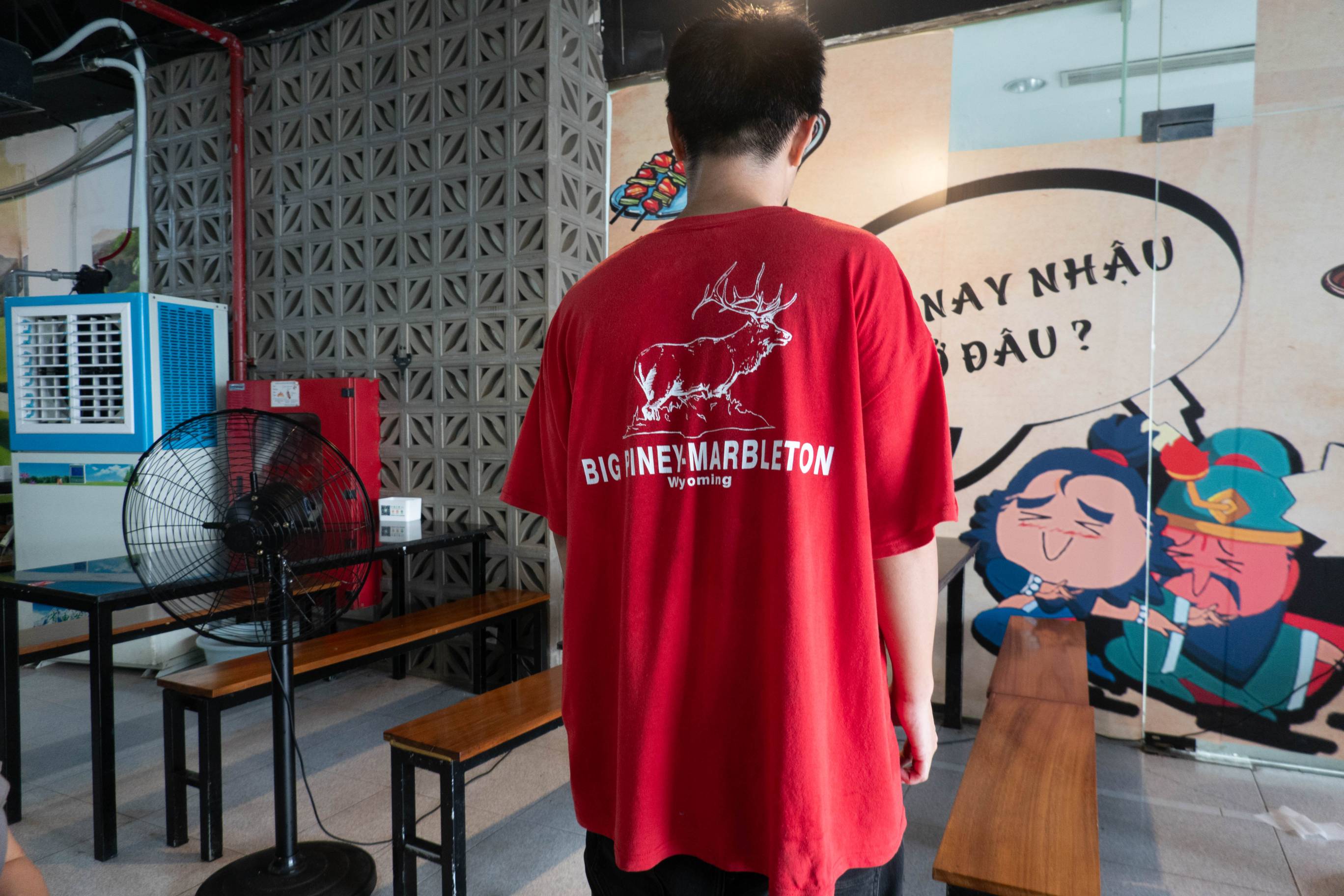 Man facing away weaing a red t-shirt. It has a picture of an elk and the words Big Piney-Marbleton, Wyoming in white.