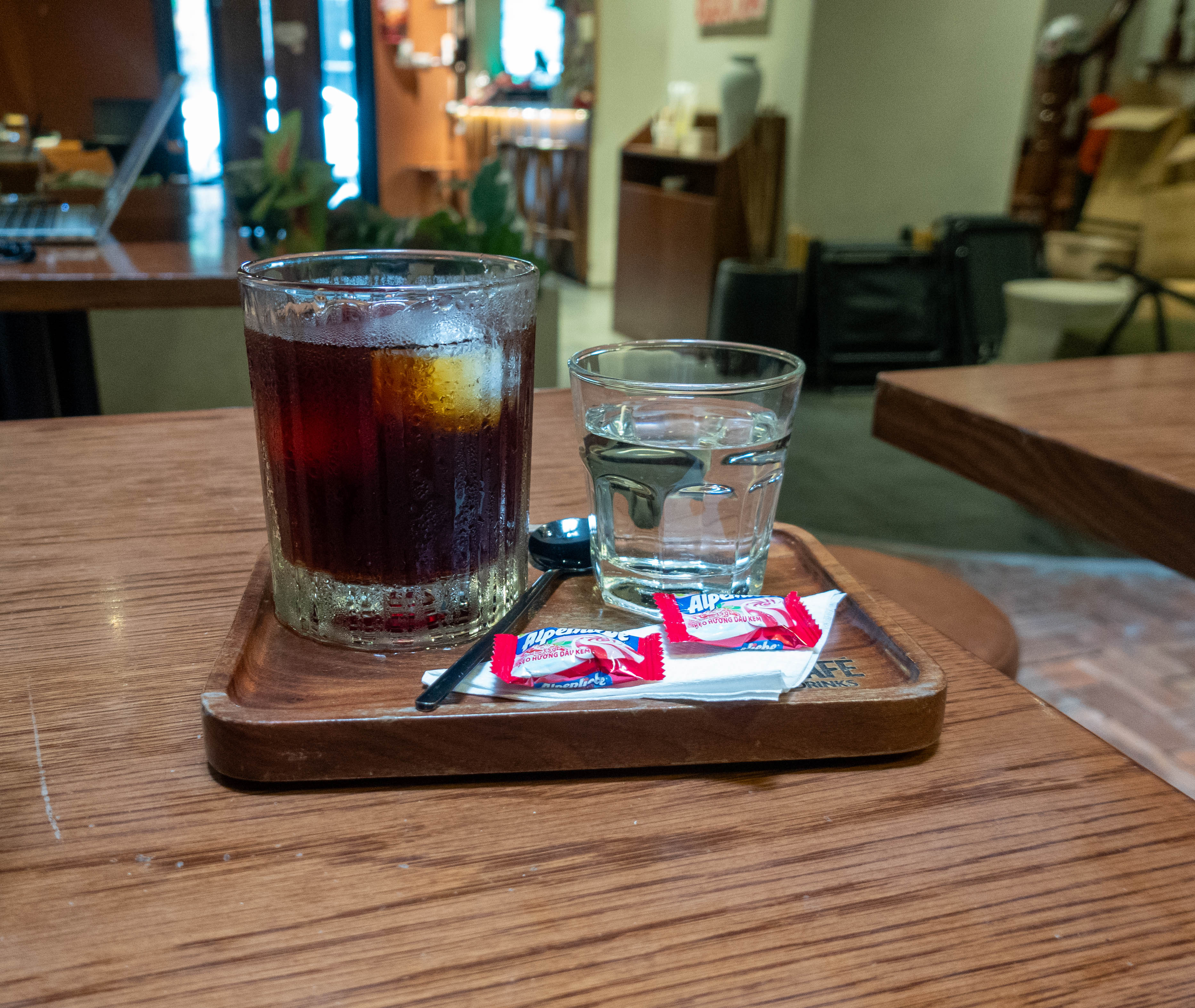 glass of ice coffee with small glass of water to the right. In from of the water sit two pieces of candy on a small napkin folded into a triangle. 