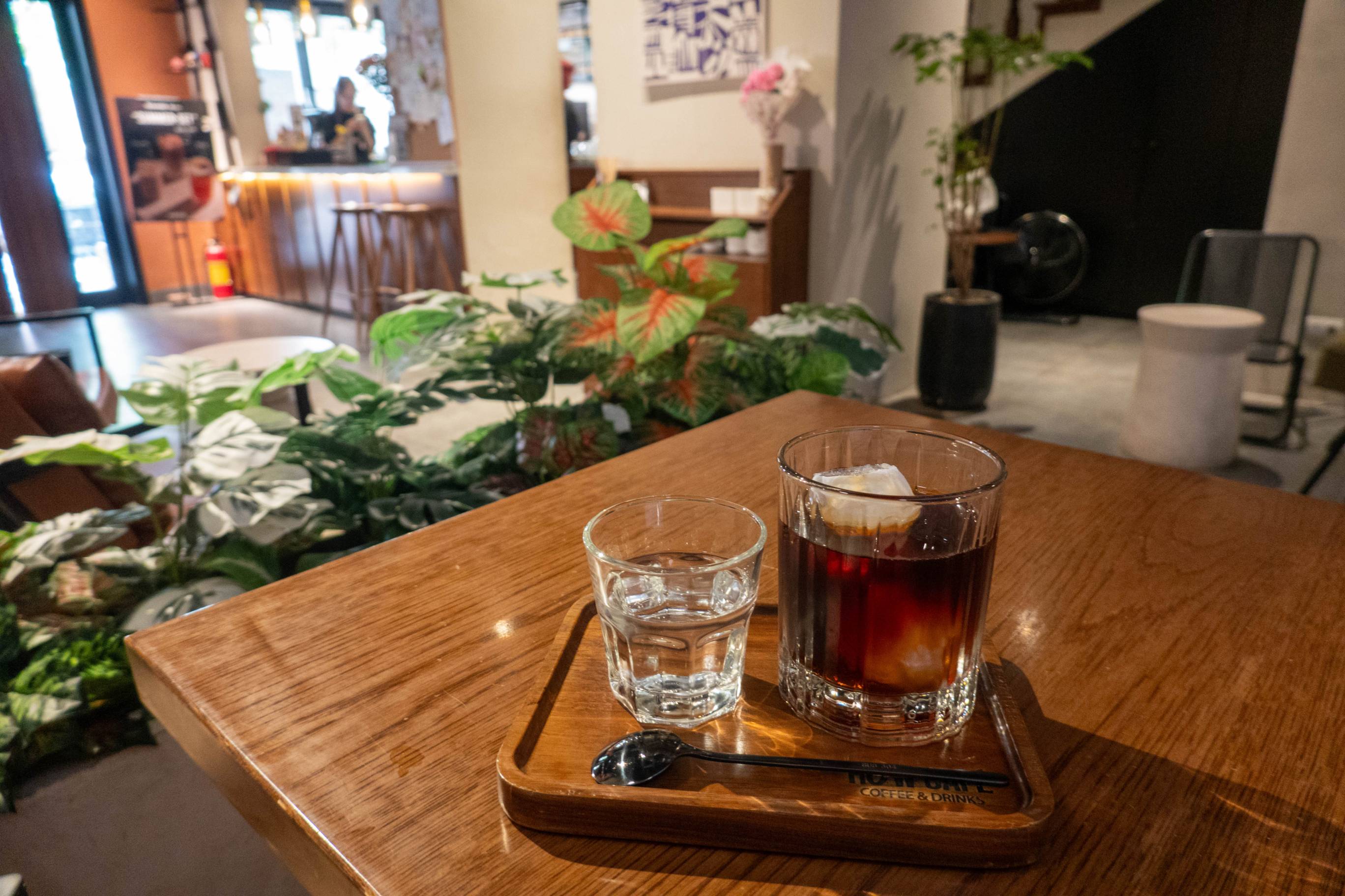 picture of small glass of water on left and larger glass of coffe on right. There is a black spoon in front of the glasses.