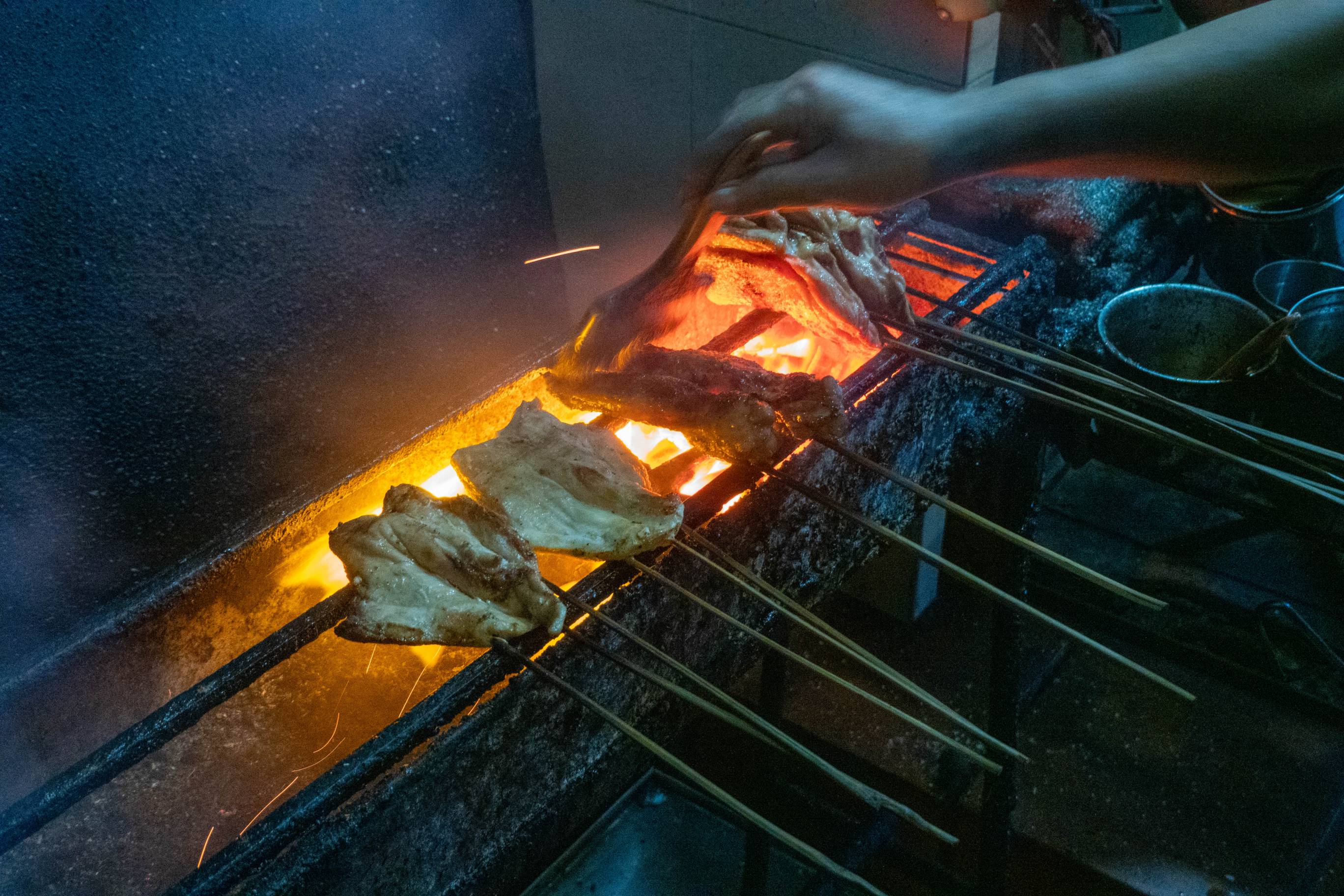 hand basting two very large extended chicken wings on skewers cooking over open pit.