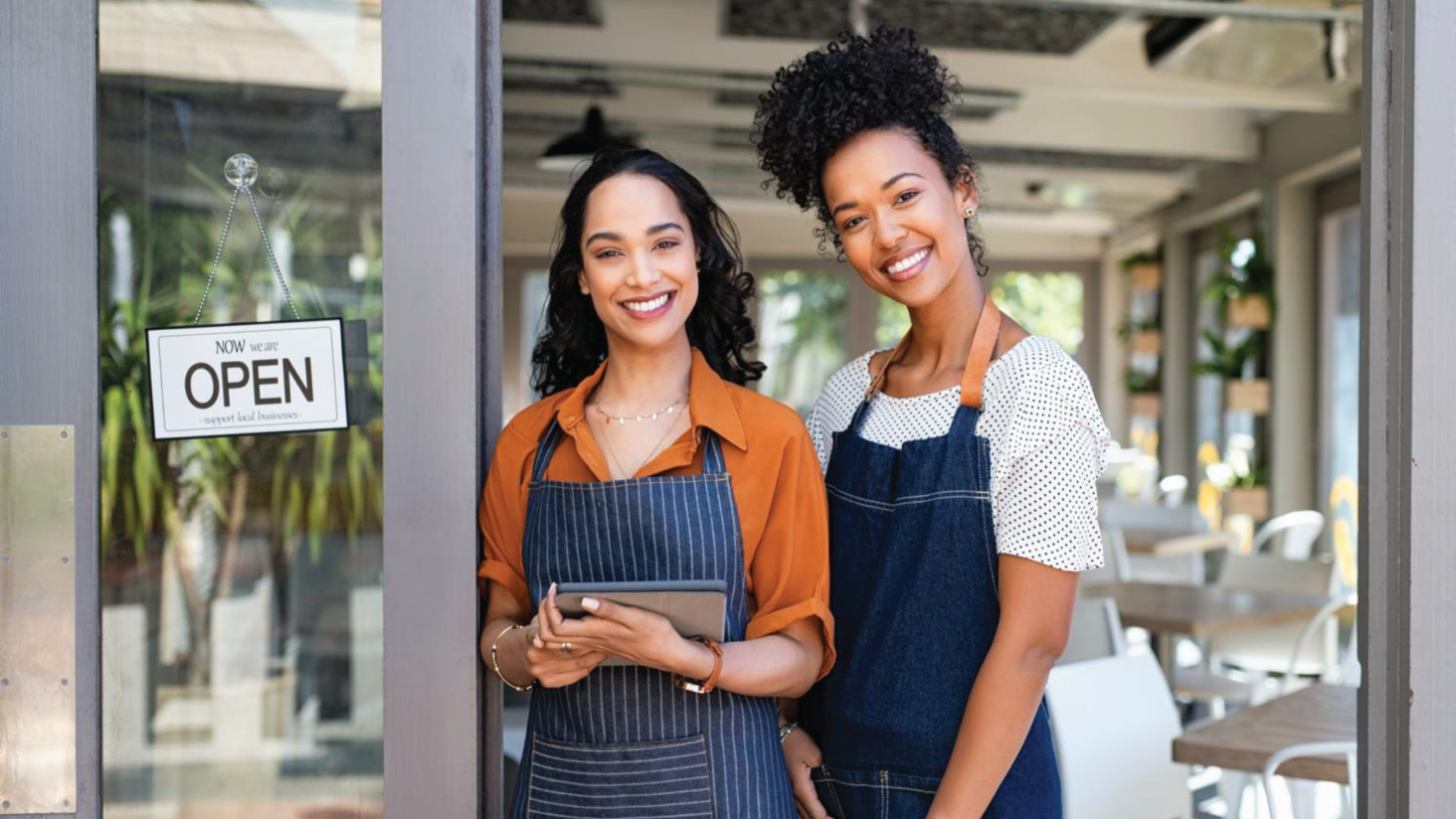 Two women business owners standing in the doorway of a restaurant smiling.