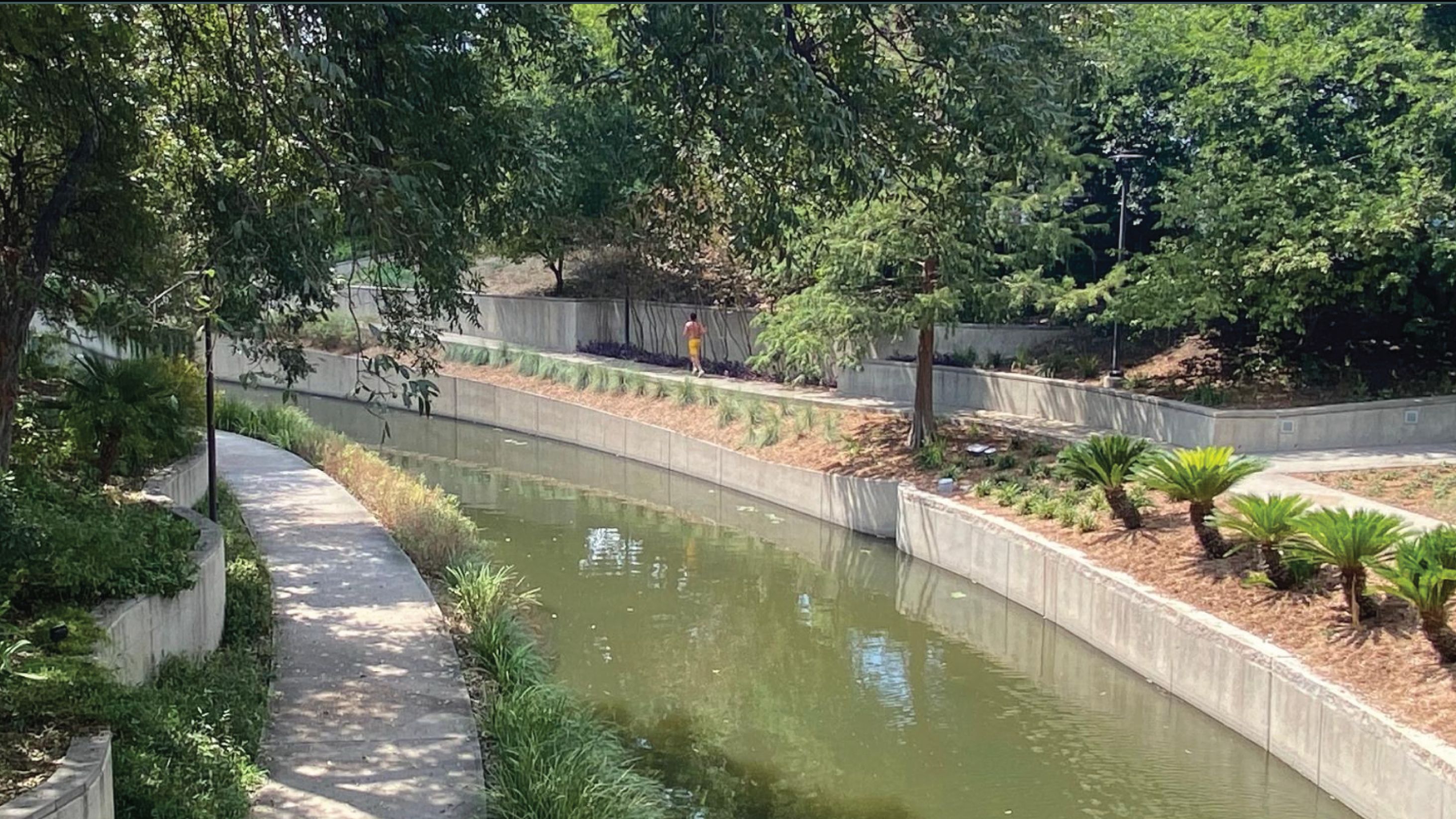 Greenery and a sidewalk can be seen on either side of a river.