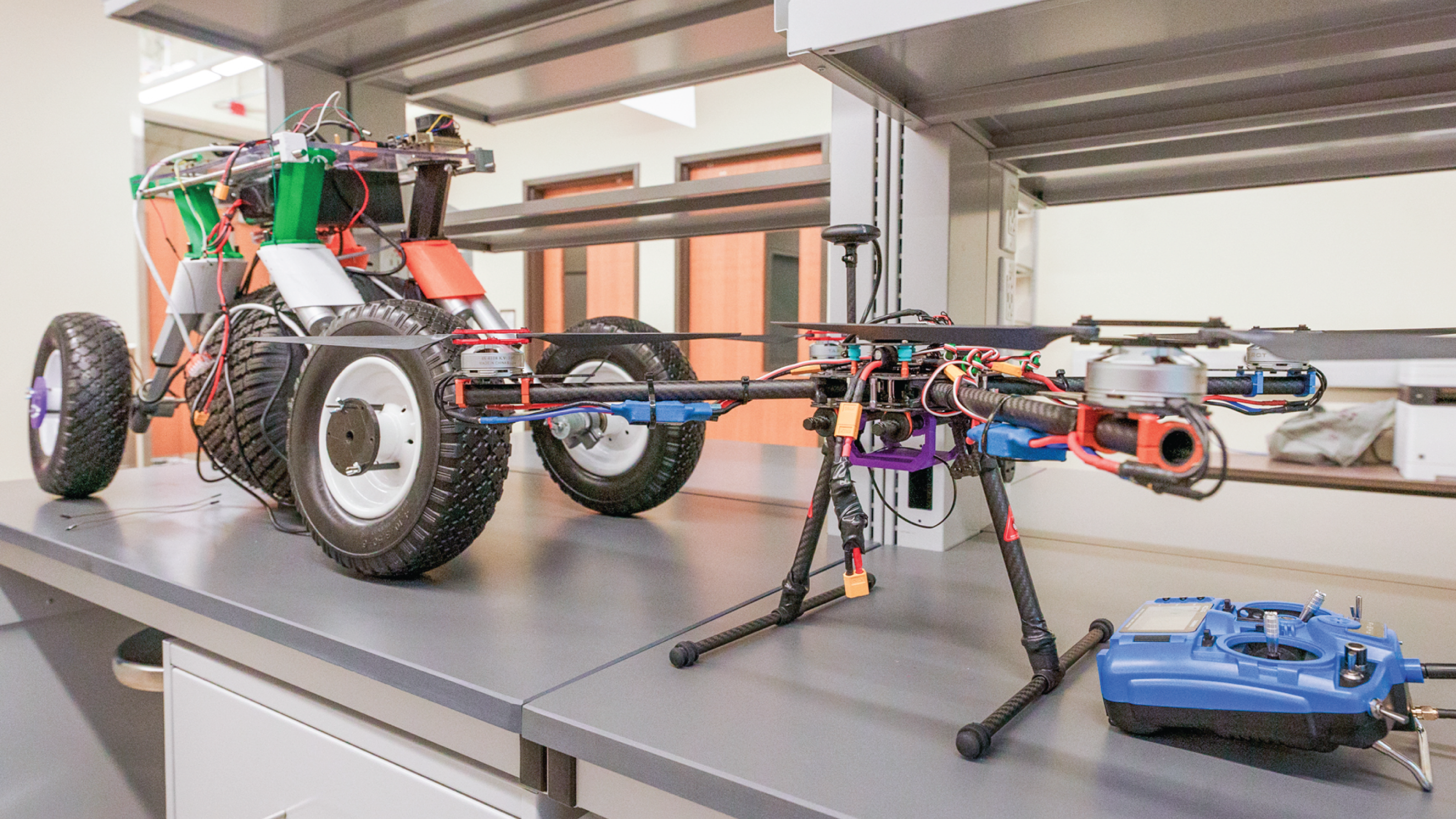 Engineered fire drone and rover sit on top of a metal lab table.