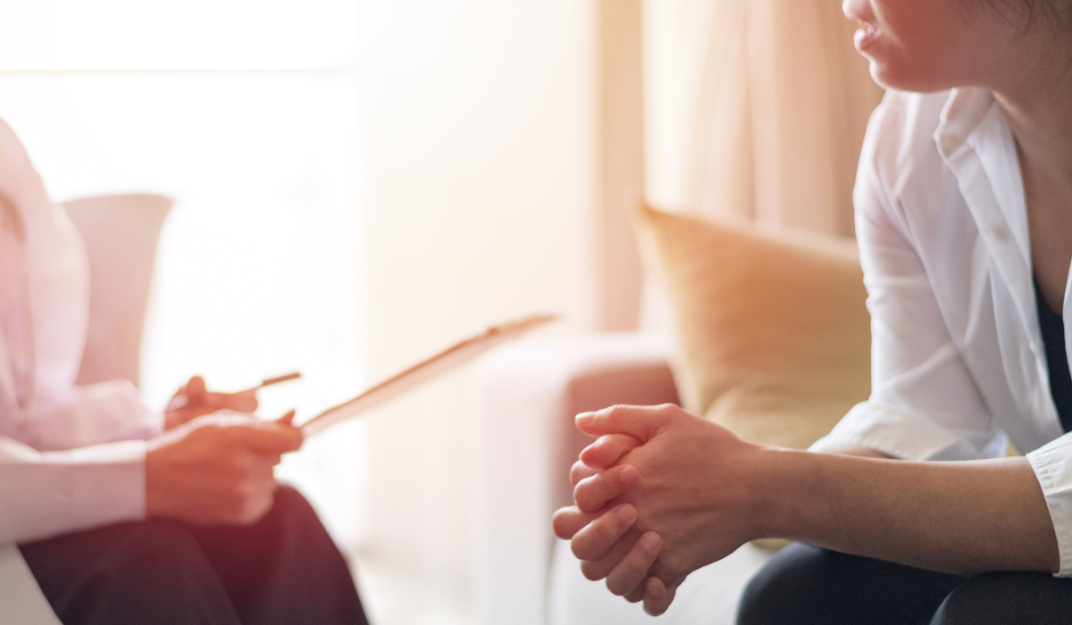 A lady with a clipboard sits and talks with another woman.