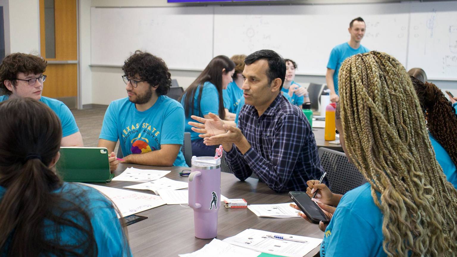 A faculty member speaks with students at a table.