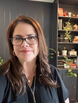 woman with glasses, bookcase with plants in background