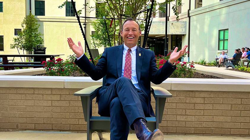 President Damphousse sits in a chair in the courtyard of the Hilltop Complex.