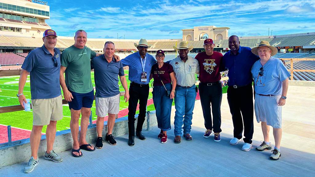 President Damphousse poses for a photo with a group at UFCU Stadium in front of the new turf.