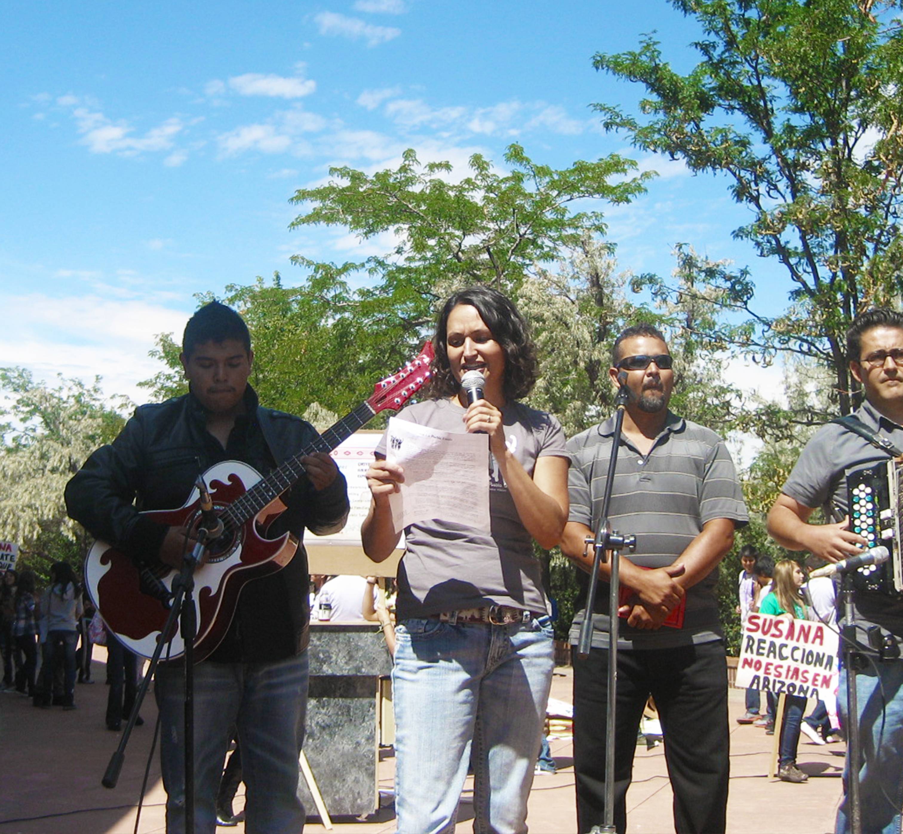 Dr. Aimee Villarreal on stage with a band reading from a paper into a microphone.