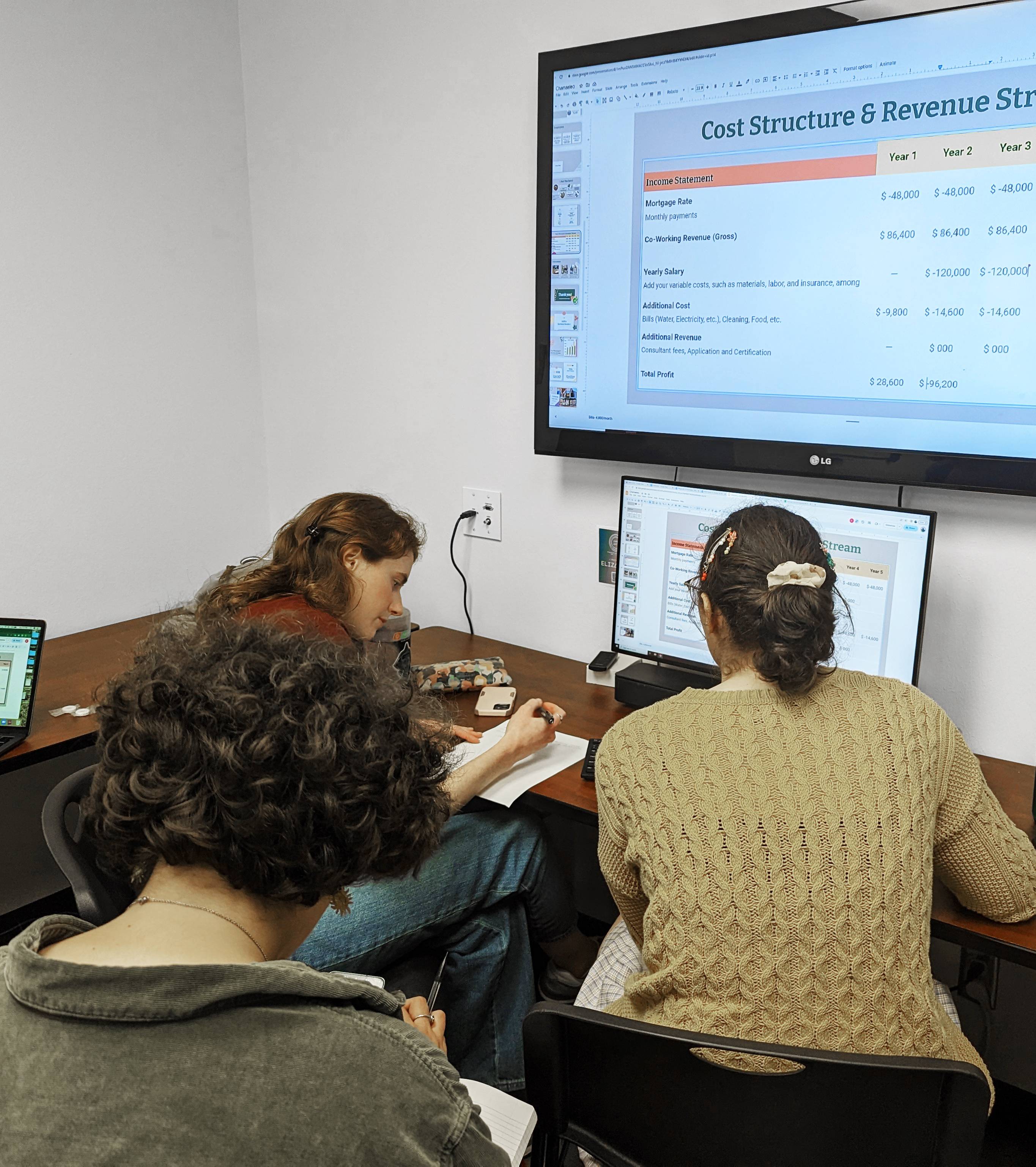 Three students sit around a computer working on a project in the lab.