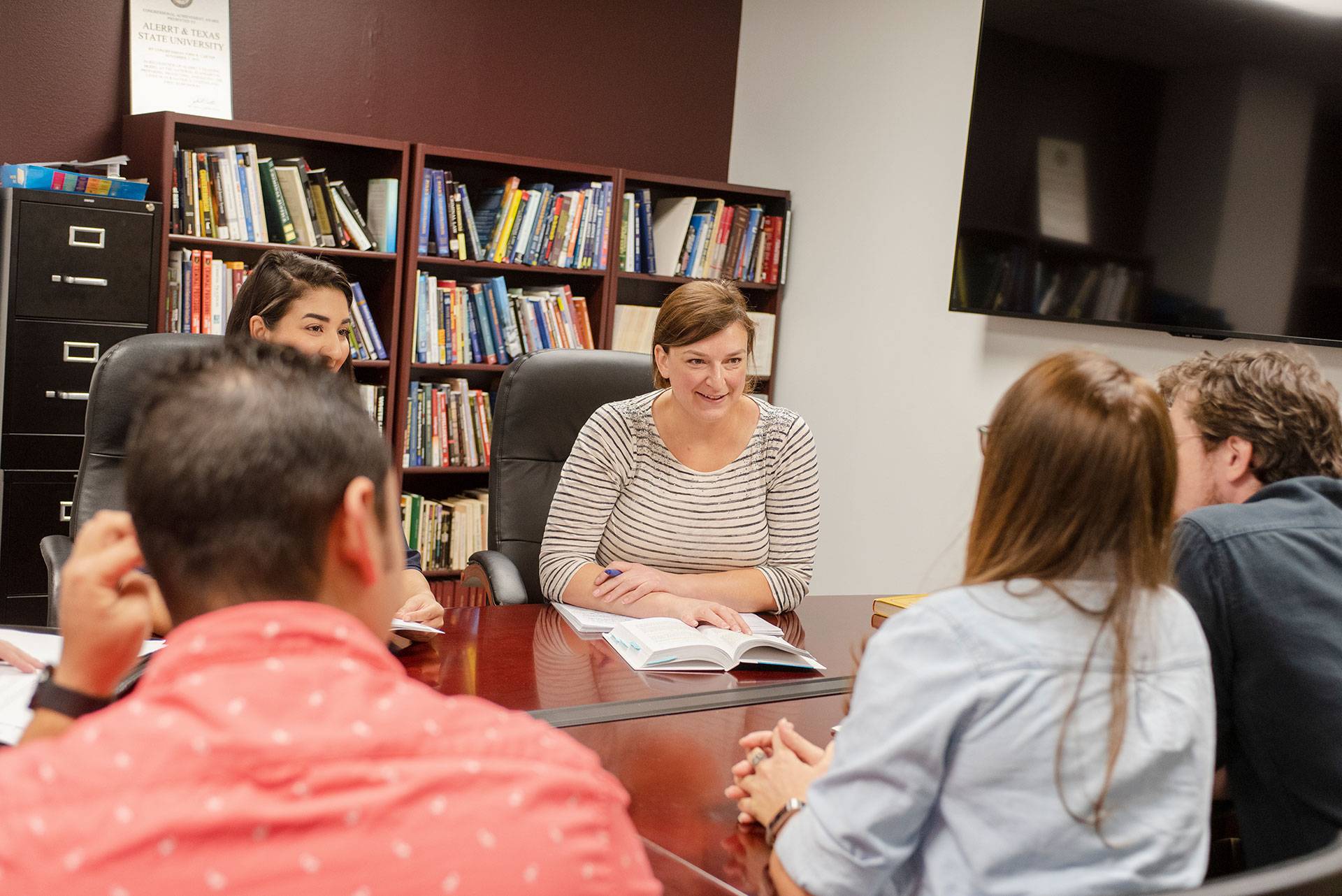 a professor leans over a table and points to something on a piece of paper as students look on