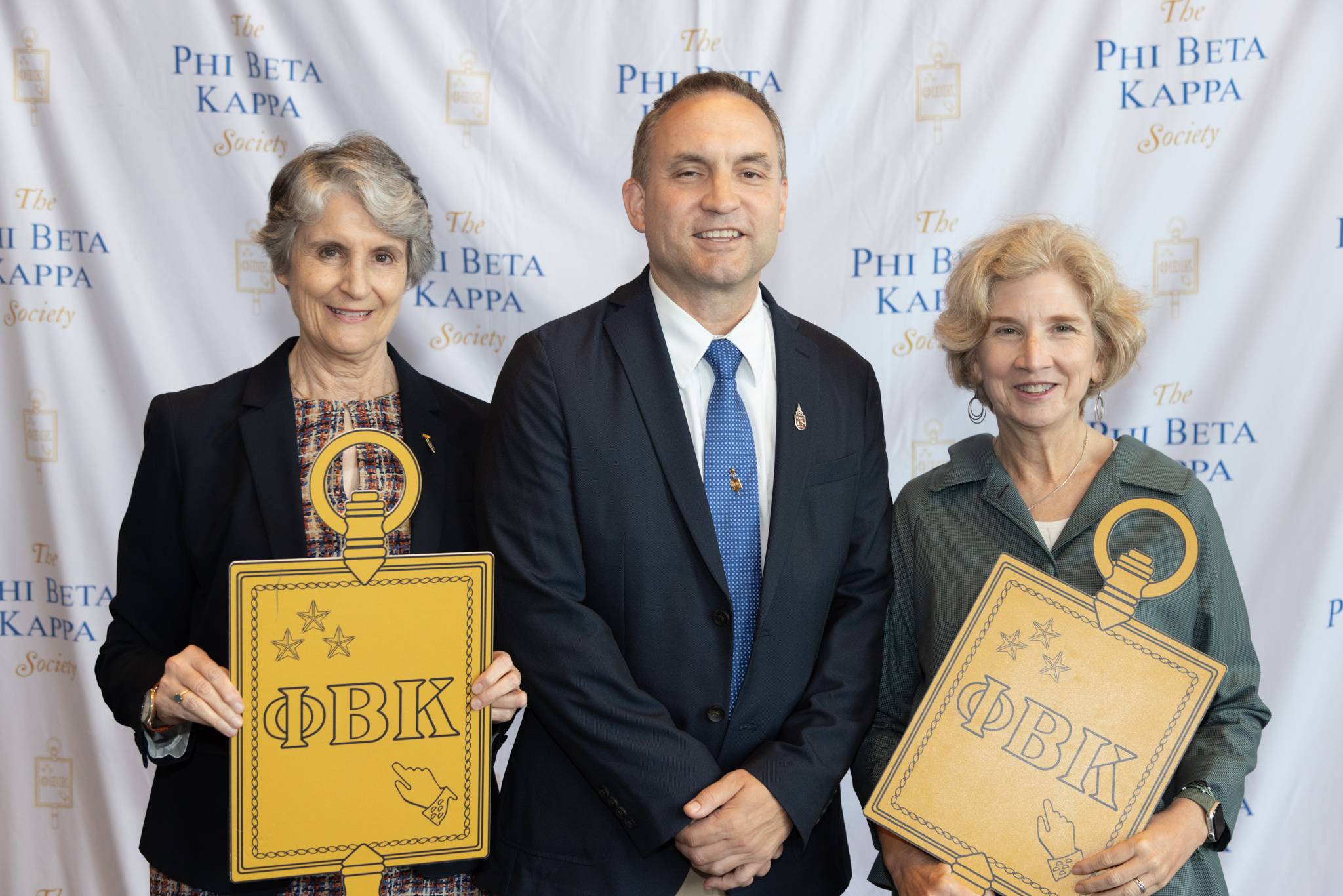 three people standing, two holding large emblems of Phi Beta Kappa