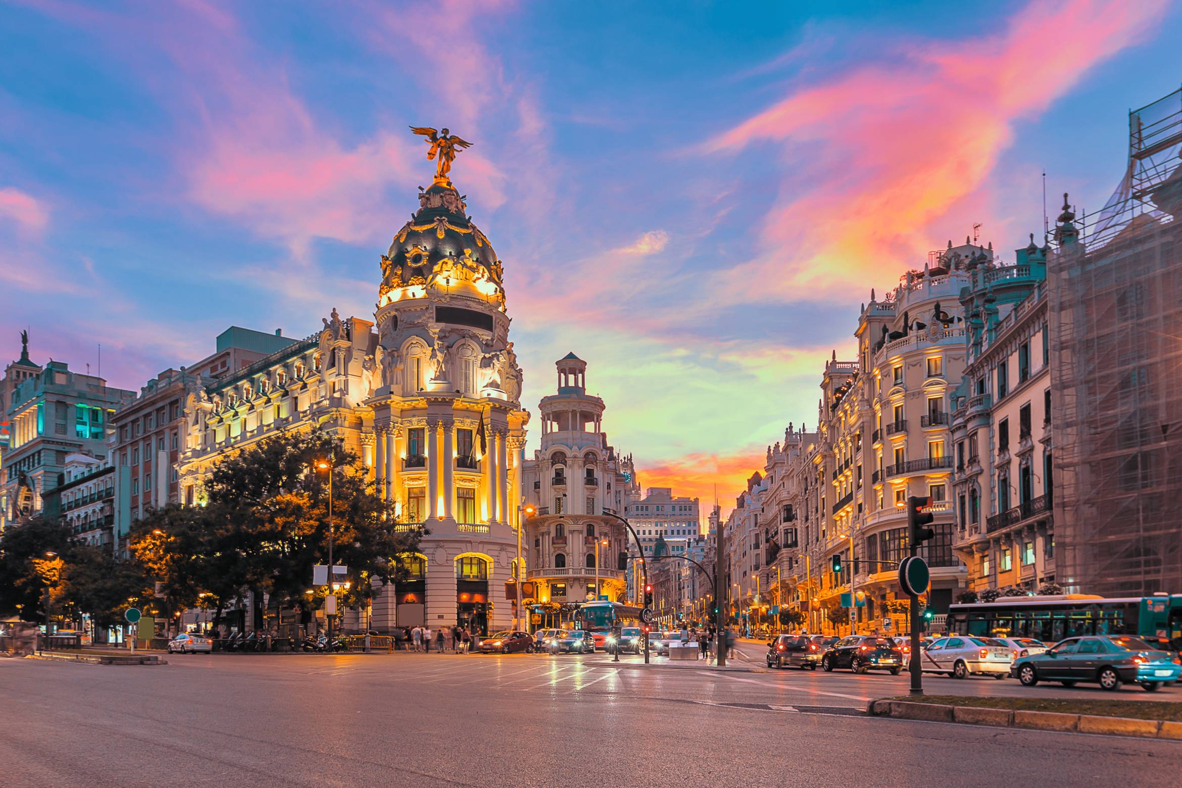 The Metropolis Building, an iconic office structure in central Madrid, stands majestically at the corner of Calle de Alcalá and Gran Vía, bathed in the warm glow of sunset, highlighting its intricate architecture.