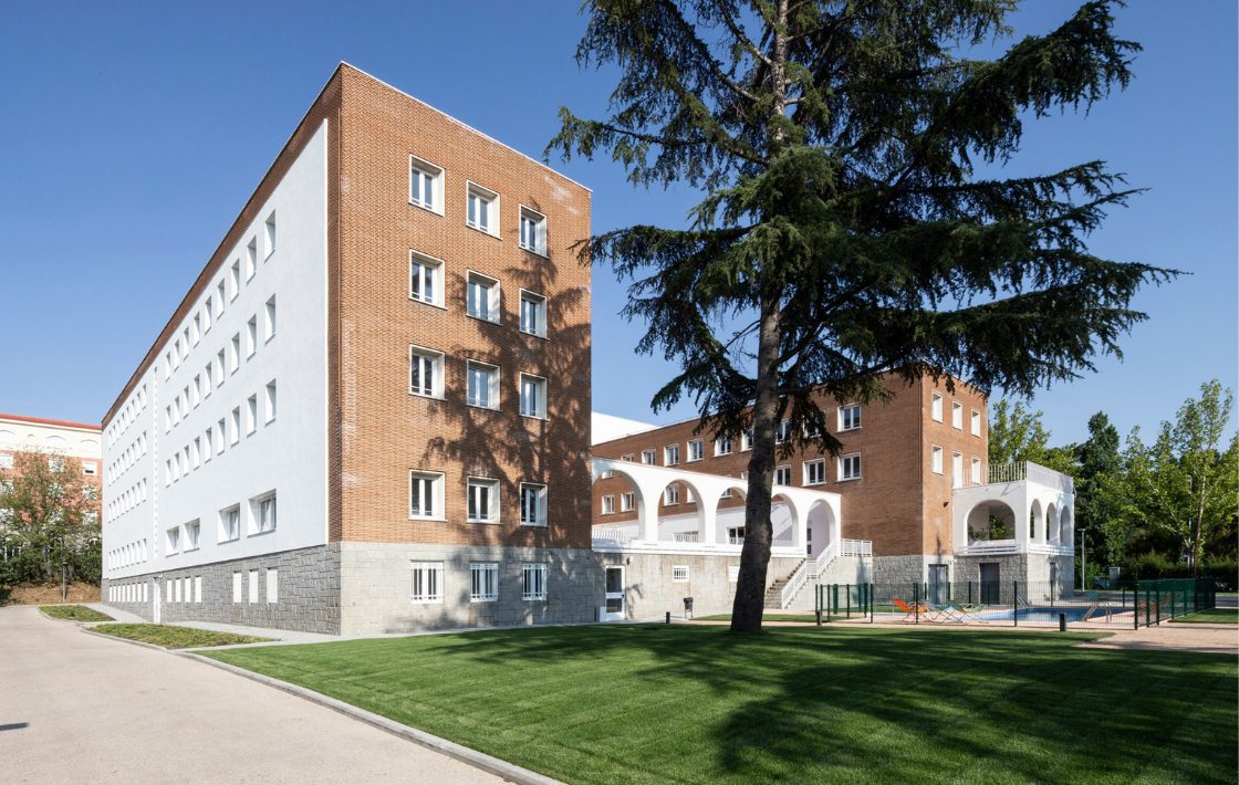 exterior view of five story Residency Hall Mayor Miguel Antonio Caro with surrounding trees, a grass lawn, and gated residential swimming pool.