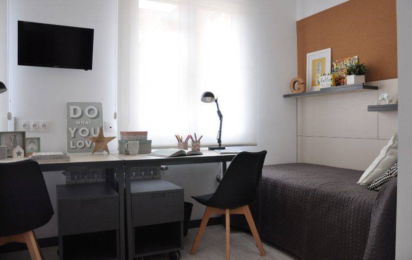 view of Residence Hall Mayor Miguel Antonio Caro's decorated bedroom; including a desk with two chairs facing the back wall between two beds and infront of a window.