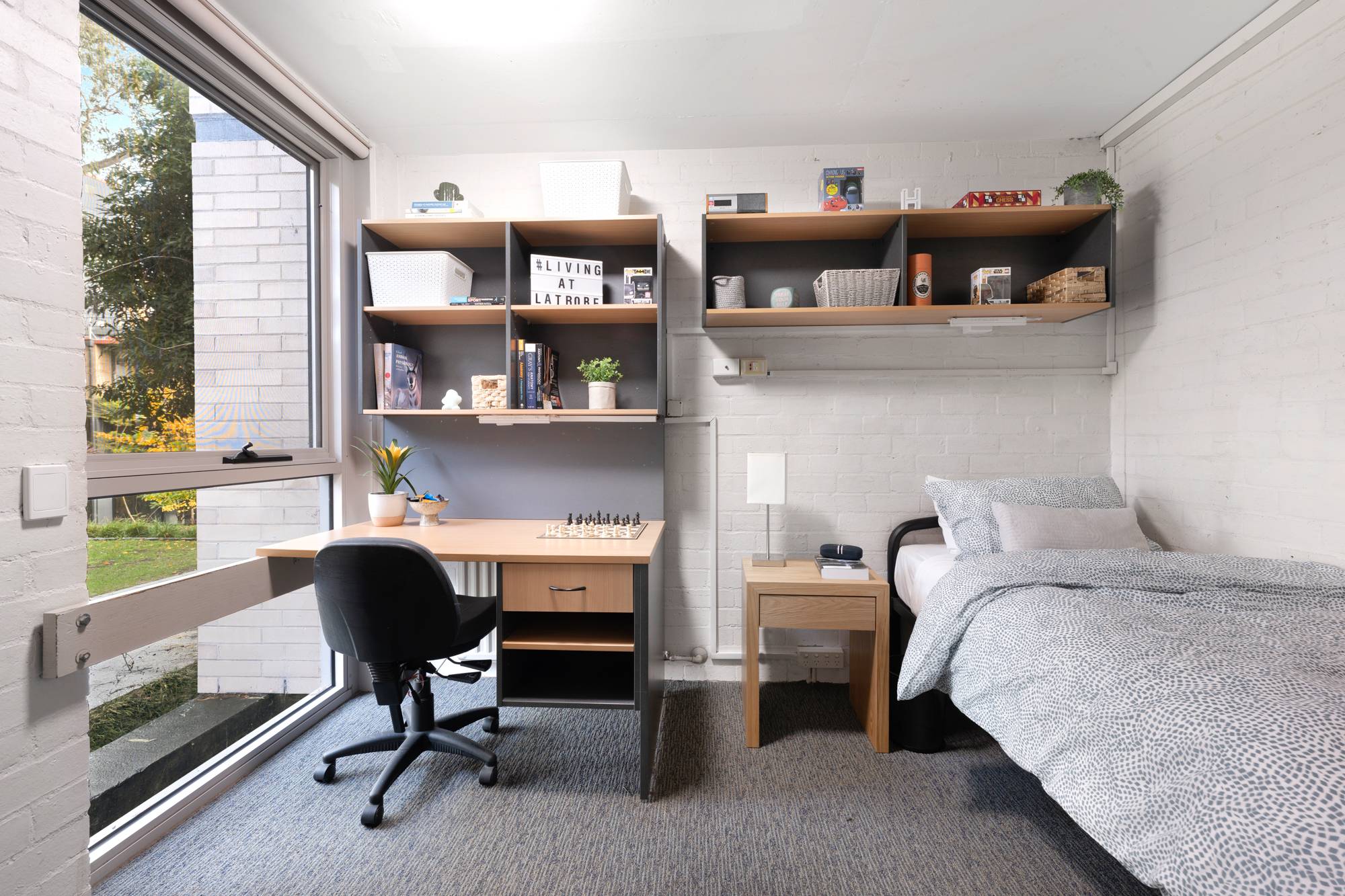 view of private bedroom with a bed, desk, and furniture with large window overlooking outside.