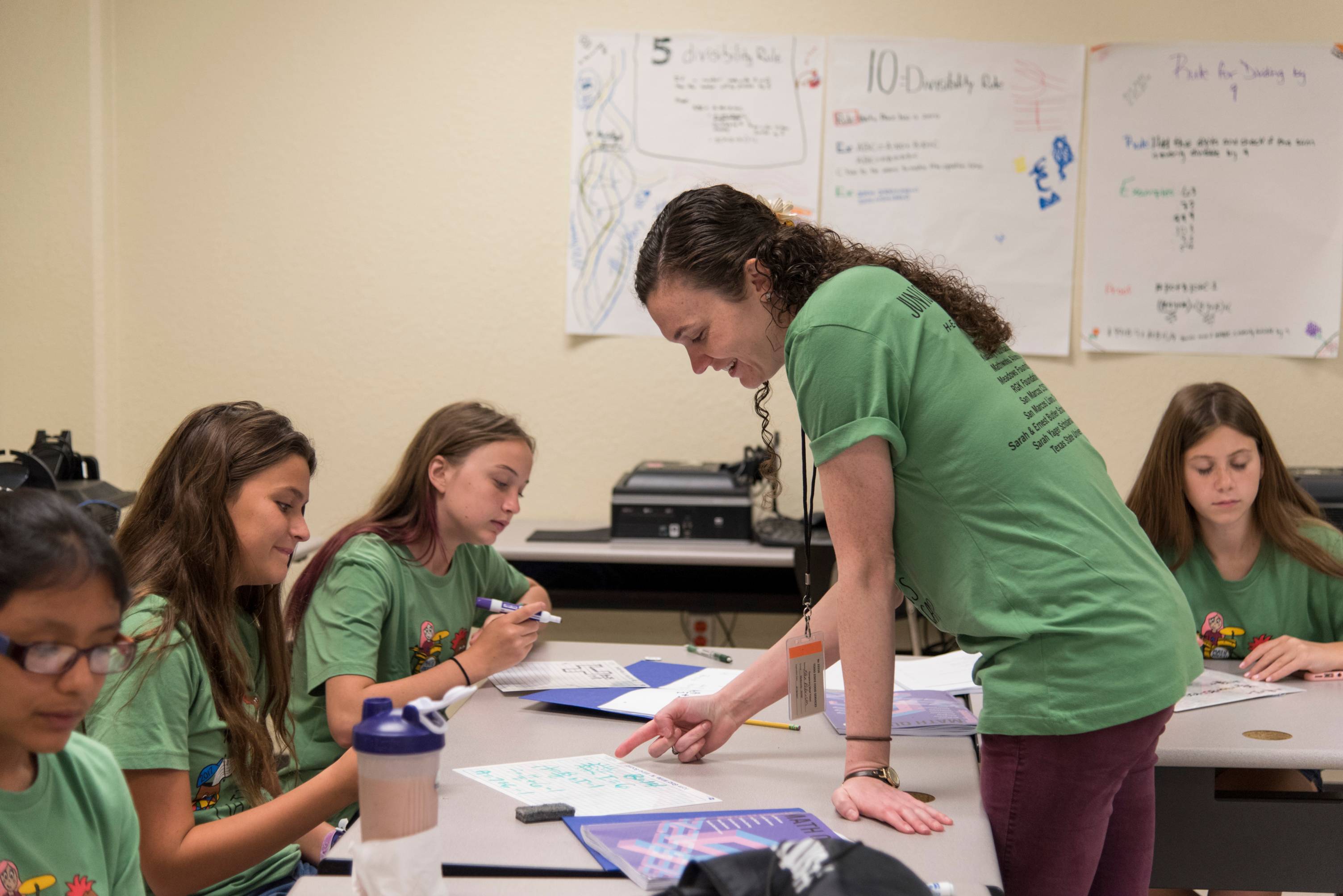 Four elementary students with desks pushed together are playing card games related to the math lesson.