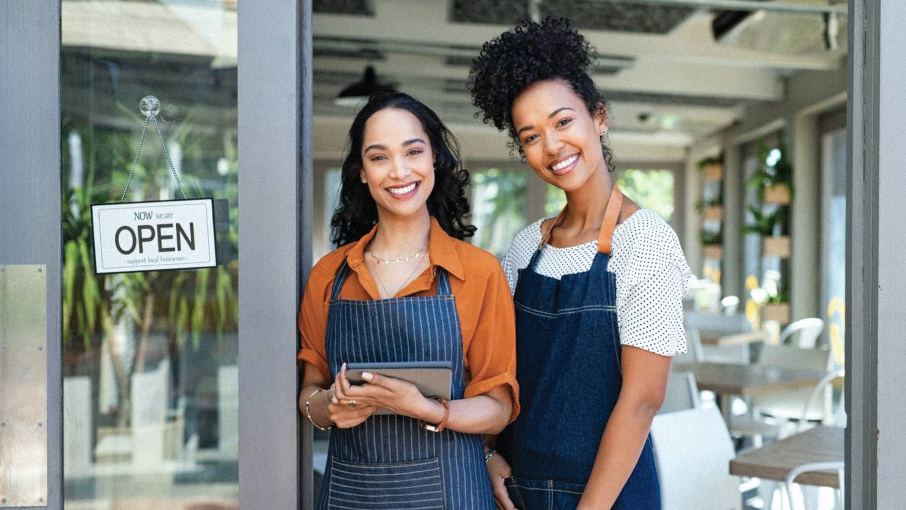 Two shop owners stand outside of their business.