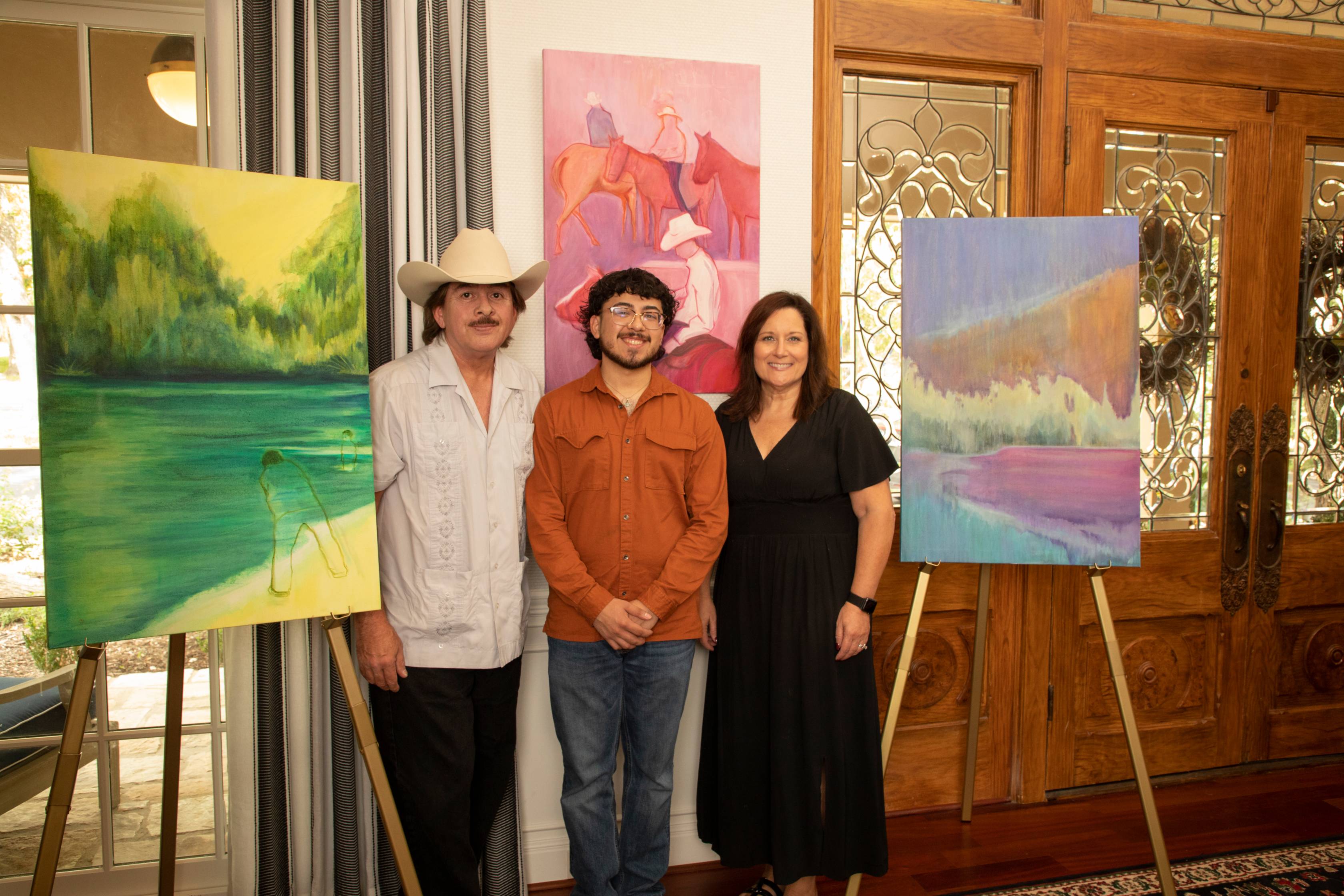 three people standing next to three oil paintings