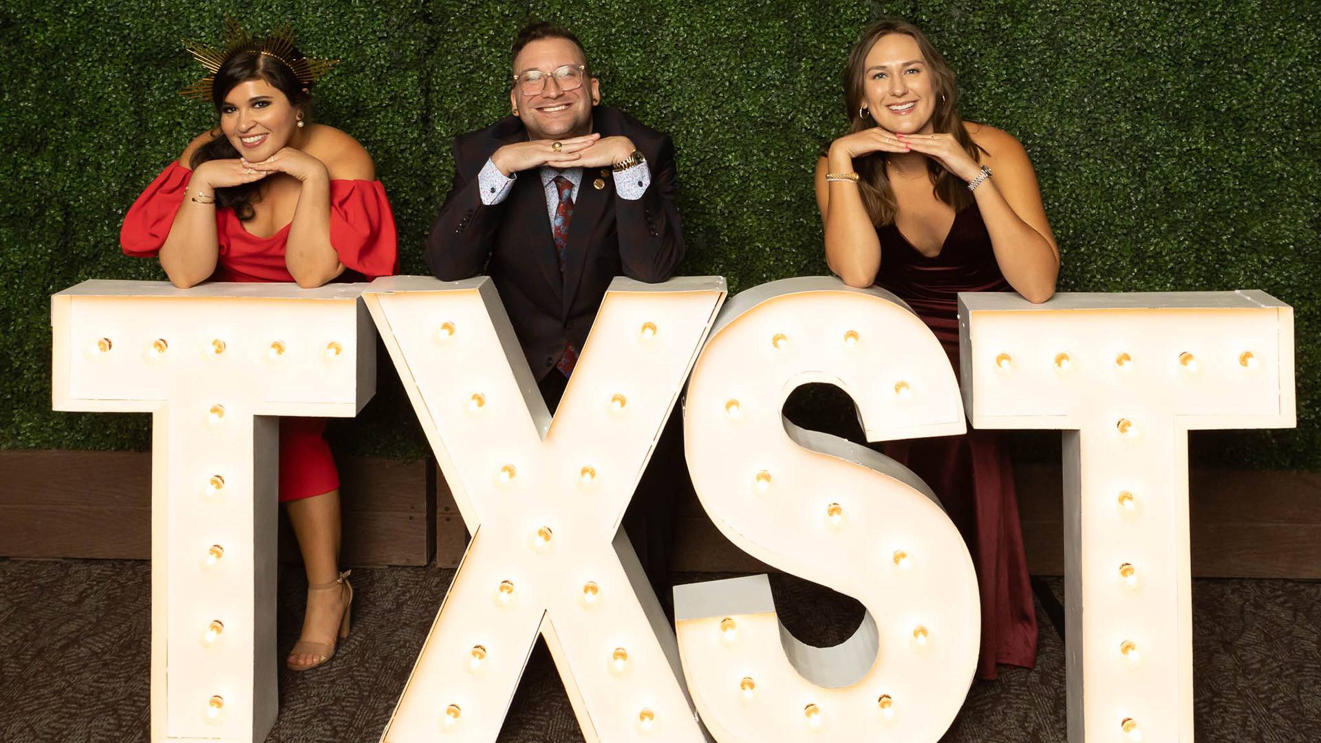 Three people smiling at Texas State sign photo backdrop at the DA gala