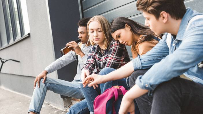 Teens sit on a curb and drink alcohol.