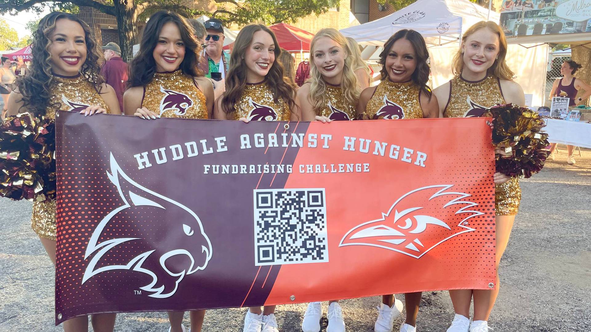 Texas State strutters holding up Huddle Against Hunger banner