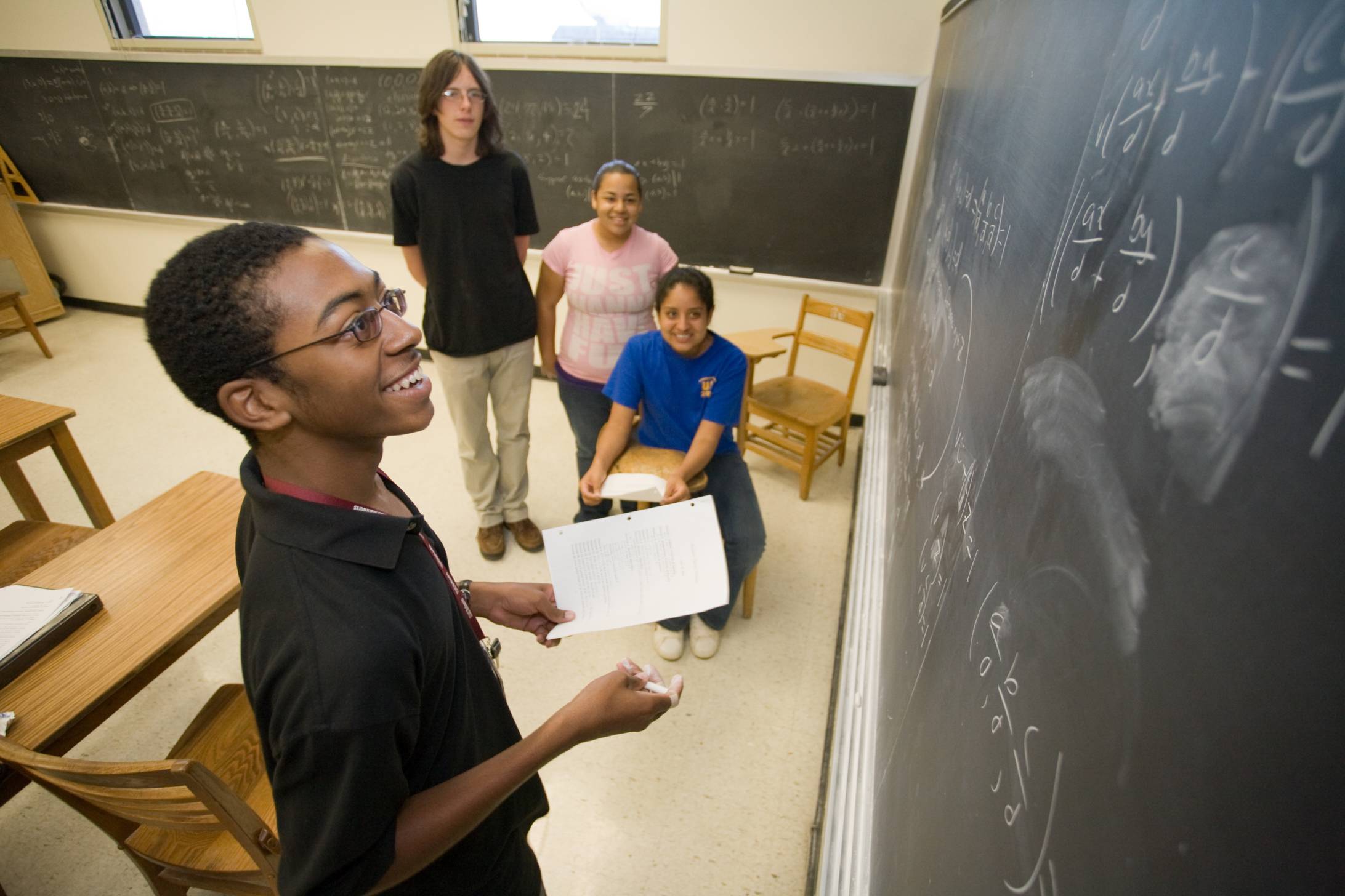 Four students with math problems on chalkboards beside and behind them. Happily solving problems together. at chalkboard