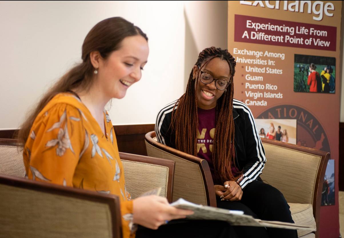 Two students are seated, speaking to each other